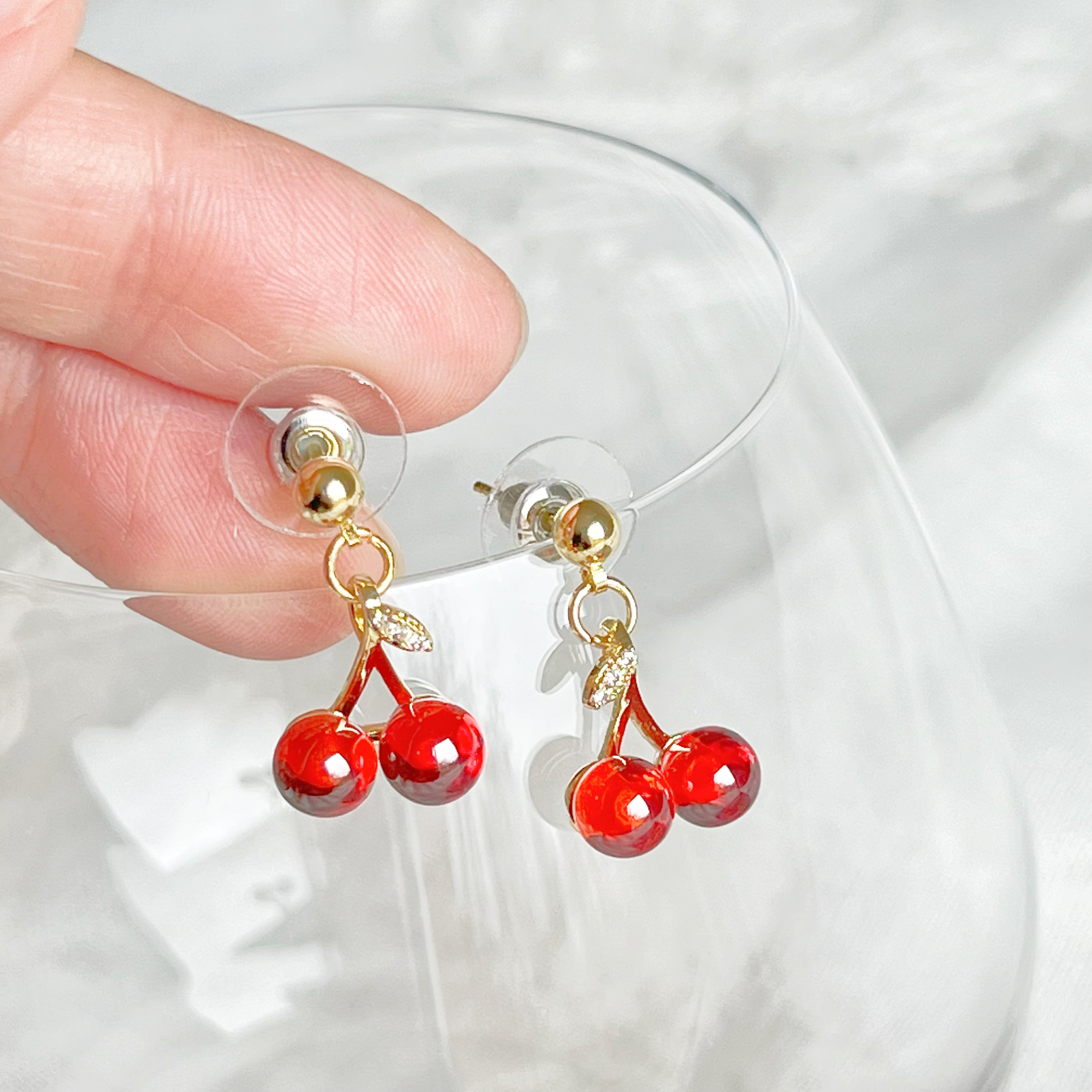 A pair of elegant Red Cherry Mini Drop Earrings featuring red zircon cherries and clear zircon bow ties, set on a gold-plated bronze base.