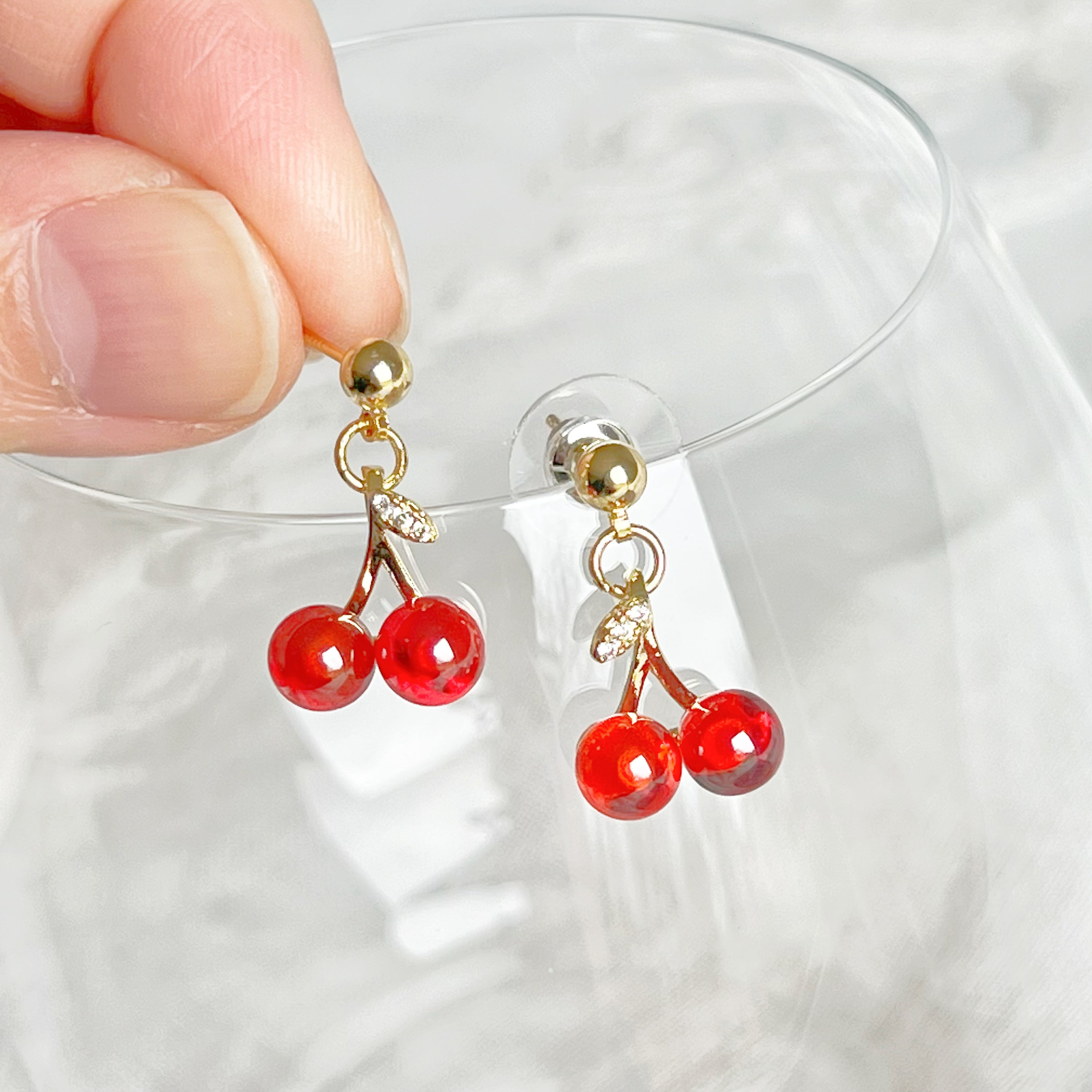 A pair of elegant Red Cherry Mini Drop Earrings featuring red zircon cherries and clear zircon bow ties, set on a gold-plated bronze base.