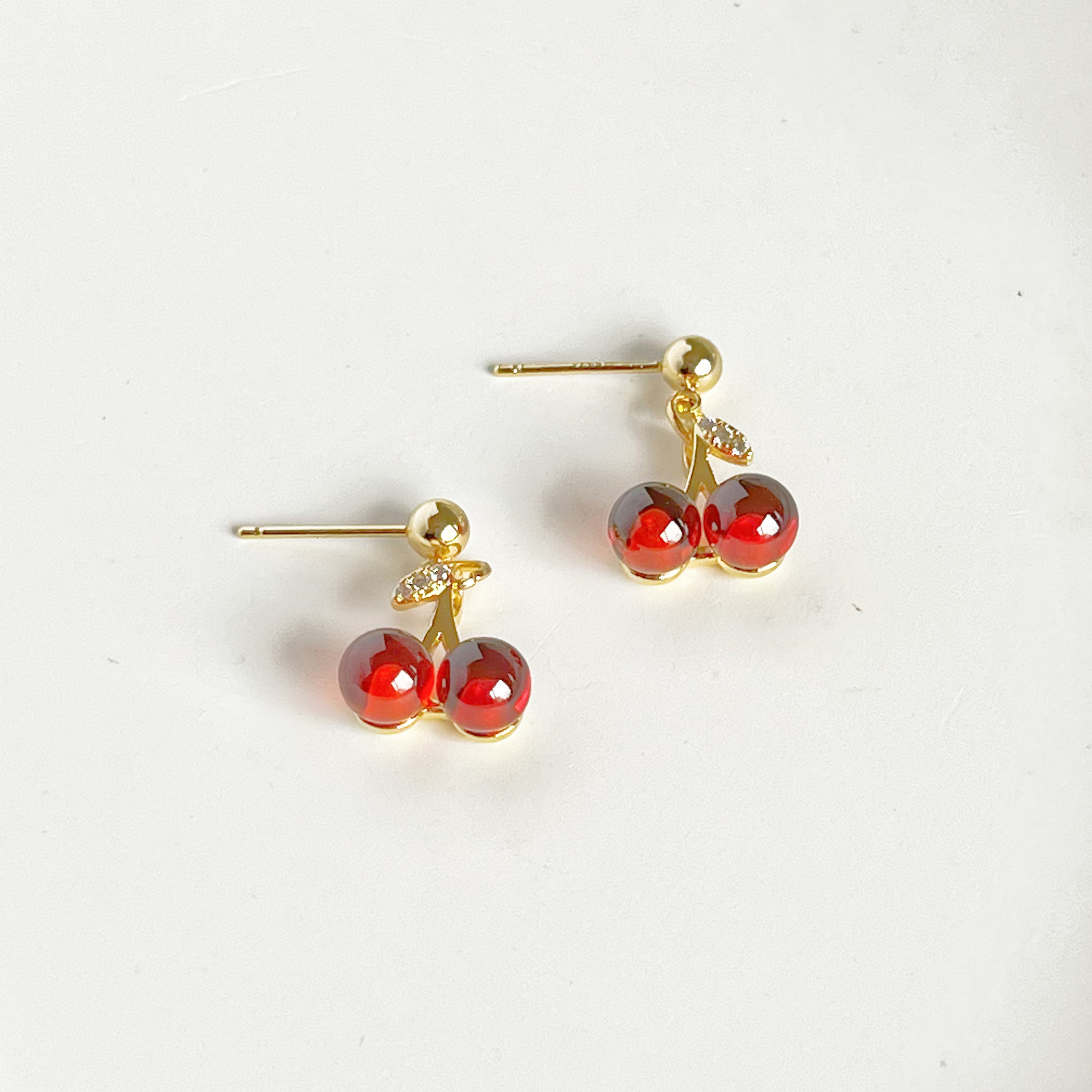 A pair of elegant Red Cherry Mini Drop Earrings featuring red zircon cherries and clear zircon bow ties, set on a gold-plated bronze base.