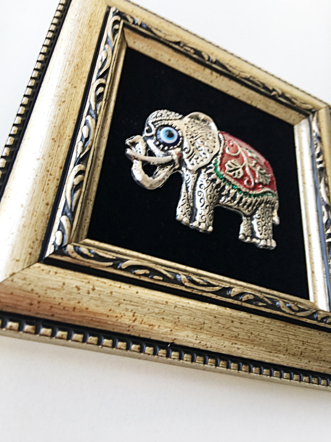 A handmade Red Elephant Frame Wall Hanging featuring a silver elephant and a small evil eye bead, measuring 14cm x 14cm.