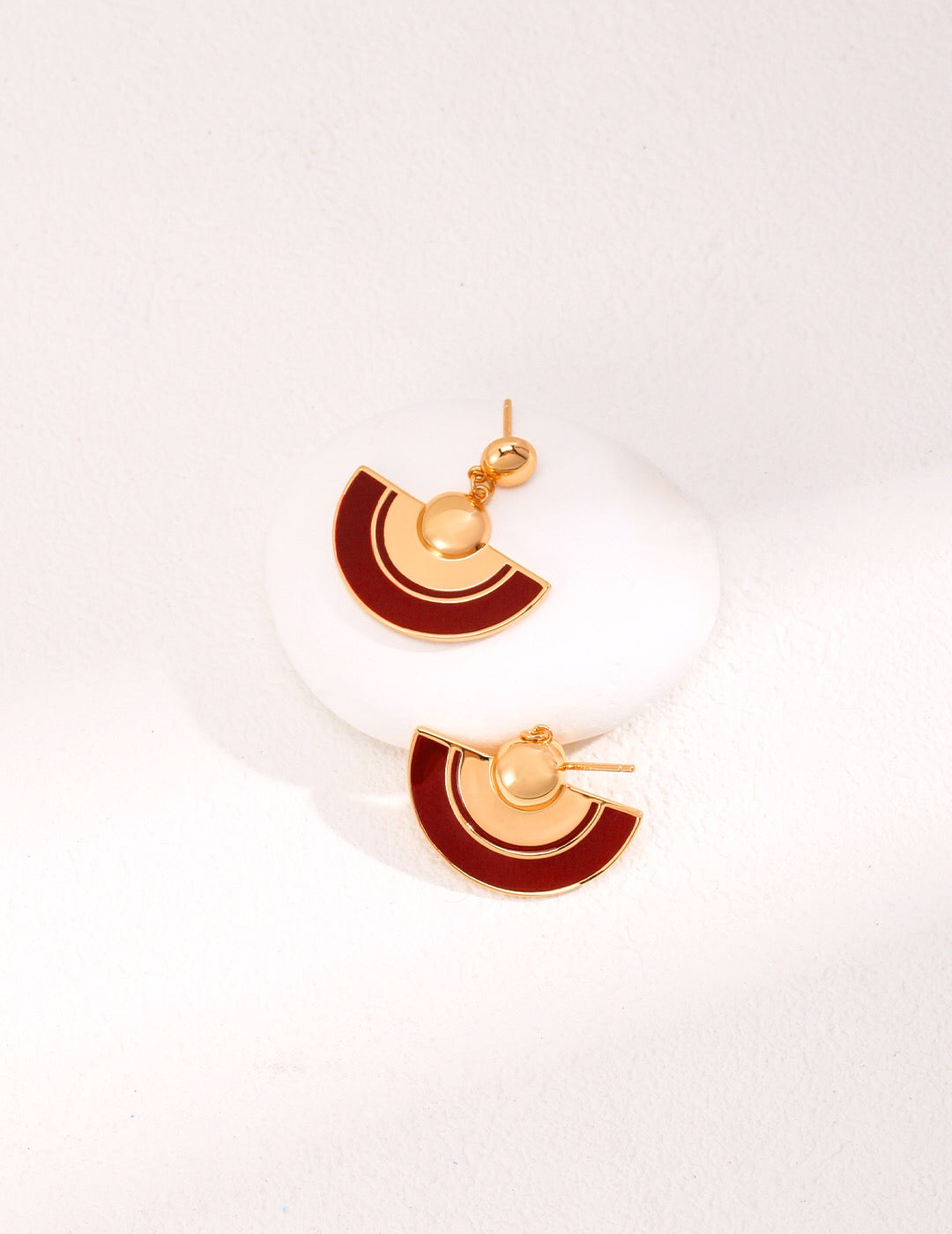 A pair of handmade red scalloped glaze earrings featuring gold vermeil accents, elegantly displayed in a jewelry pouch.