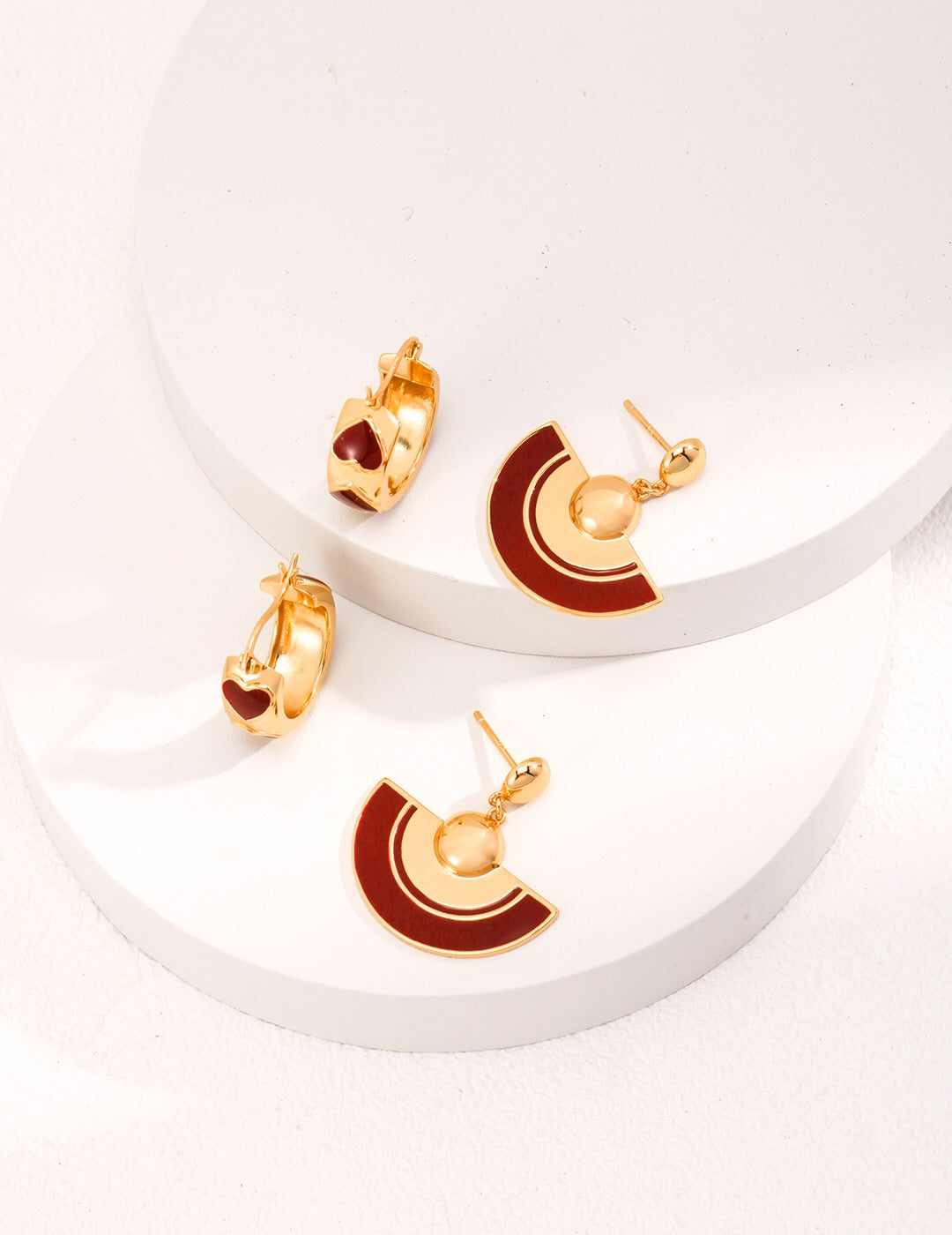 A pair of handmade red scalloped glaze earrings featuring gold vermeil accents, elegantly displayed in a jewelry pouch.