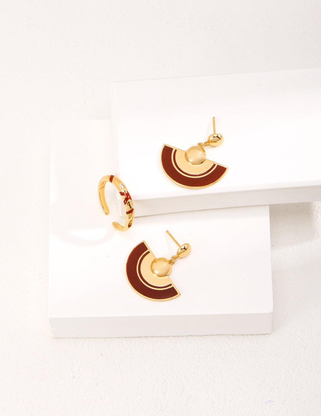 A pair of handmade red scalloped glaze earrings featuring gold vermeil accents, elegantly displayed in a jewelry pouch.