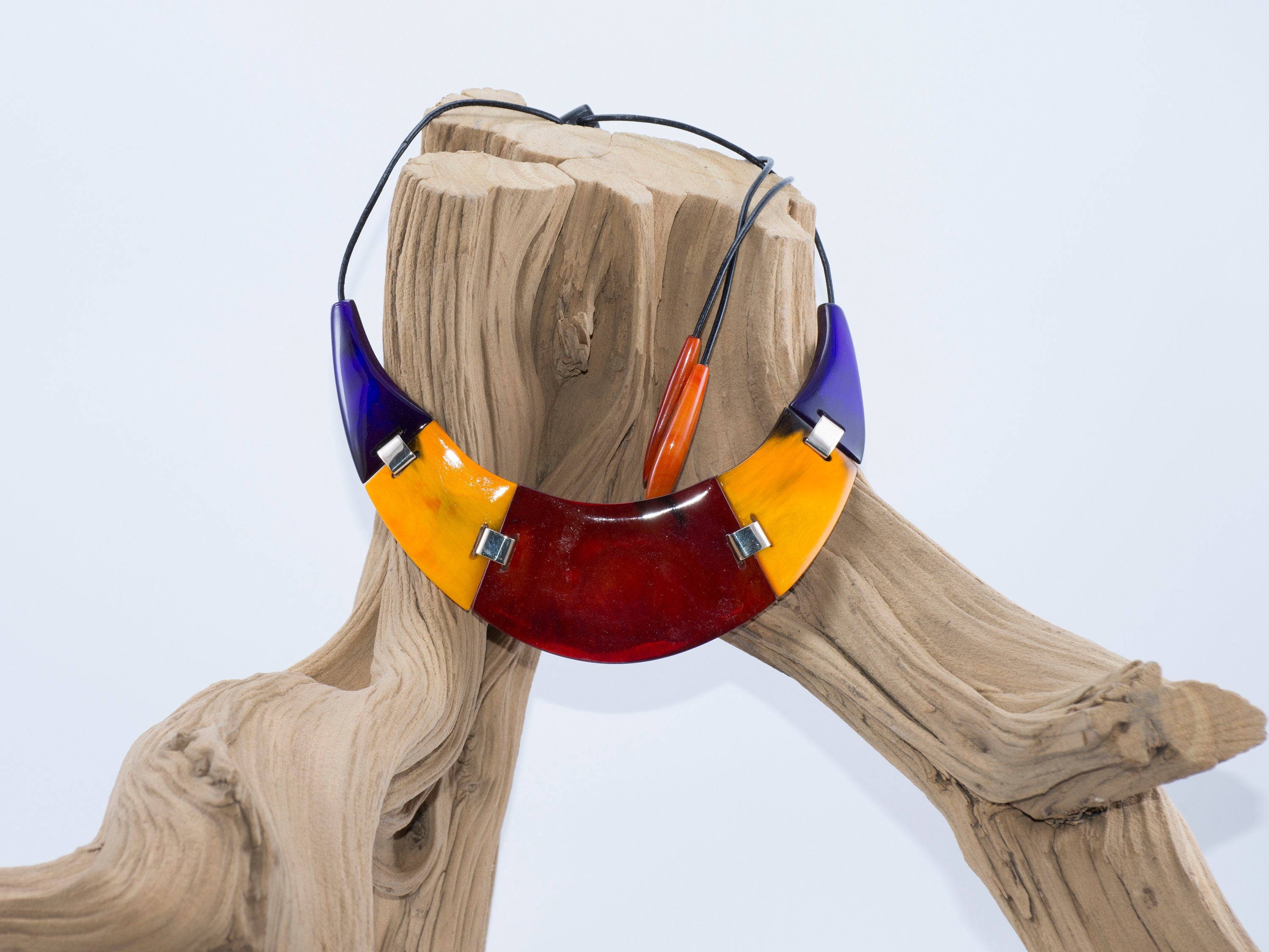 A vibrant red yellow necklace handmade from buffalo horn, featuring a unique crescent shape and adjustable length.