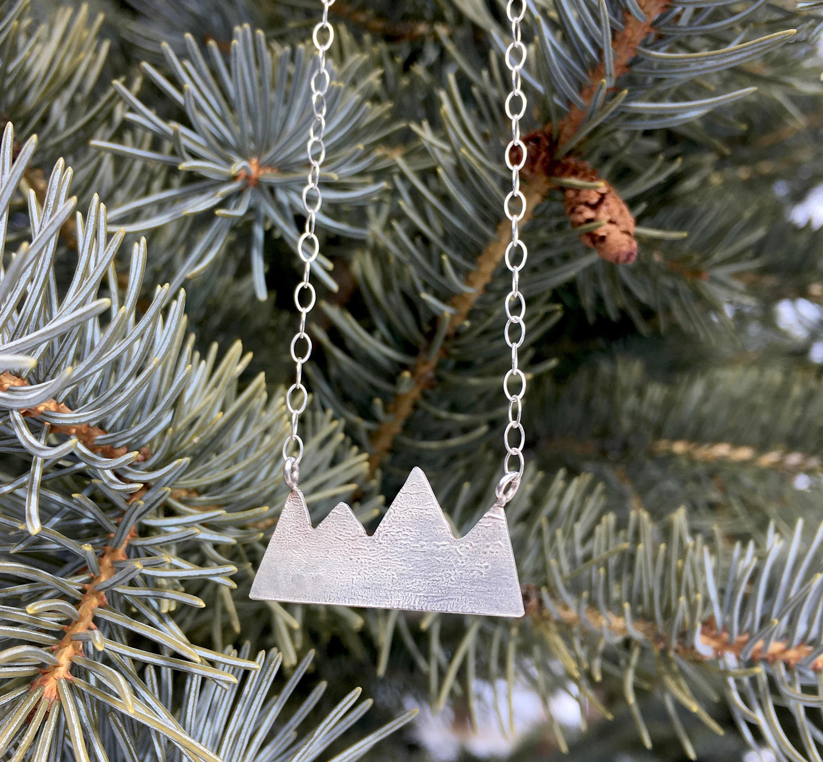 Rocky Mountains Necklace featuring a hand-cut mountain range design in reticulated silver, hanging on a sterling silver chain.