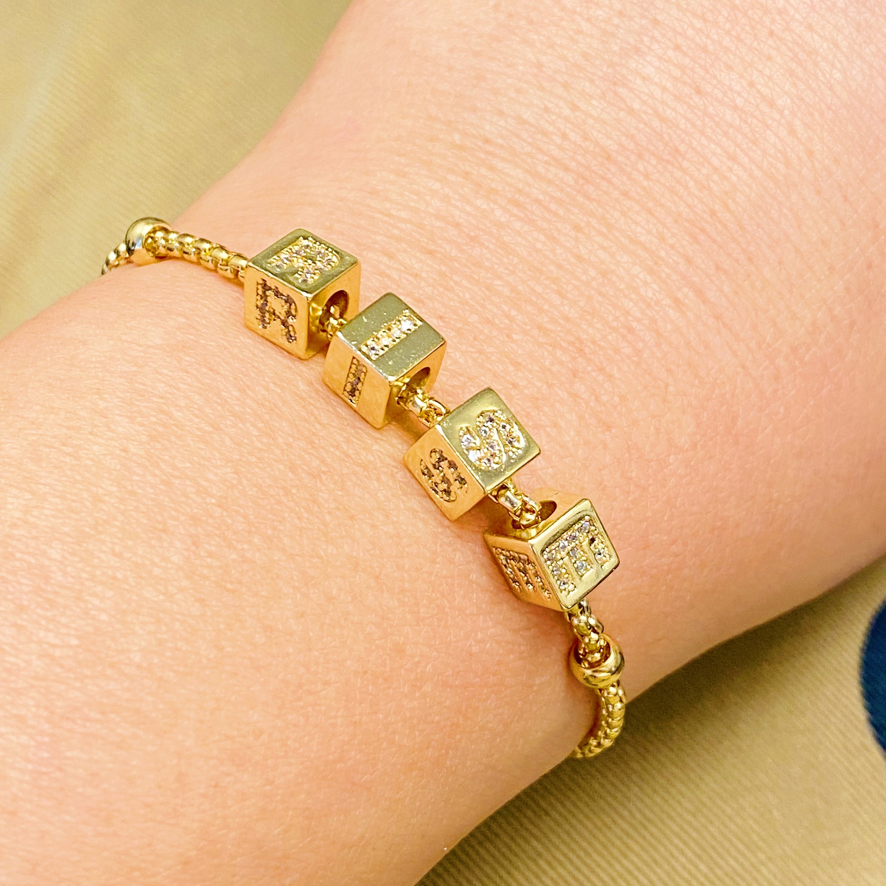 Gold plated charm bracelet featuring rolling dice with shiny paved letters and adjustable sliding chain.