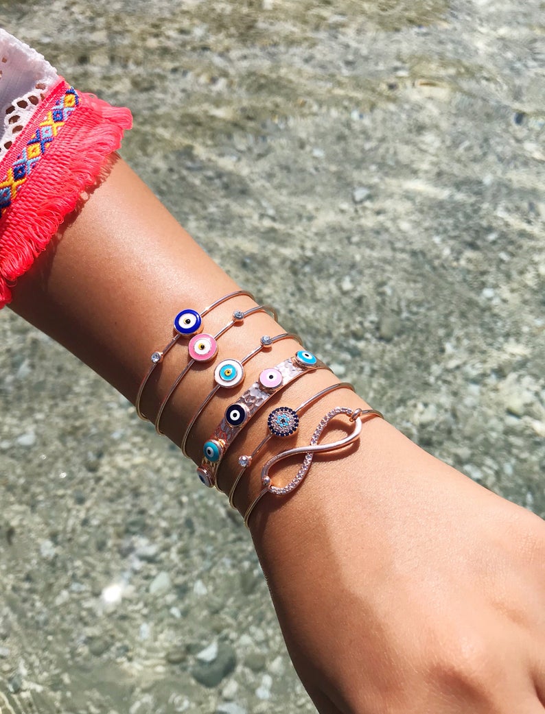 A beautiful rose gold bangle bracelet featuring a movable blue evil eye charm, showcasing its elegant design and adjustable fit.