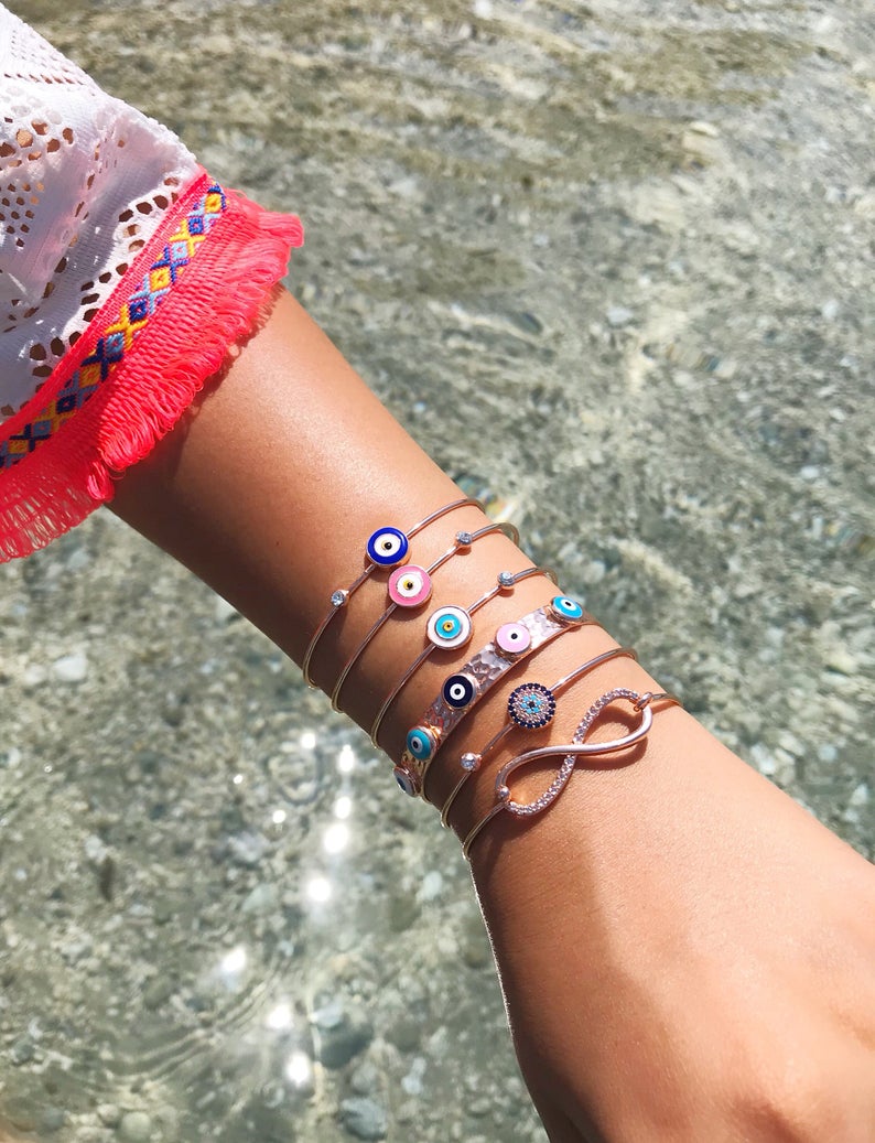 A beautiful rose gold bangle bracelet featuring a movable blue evil eye charm, showcasing its elegant design and adjustable fit.