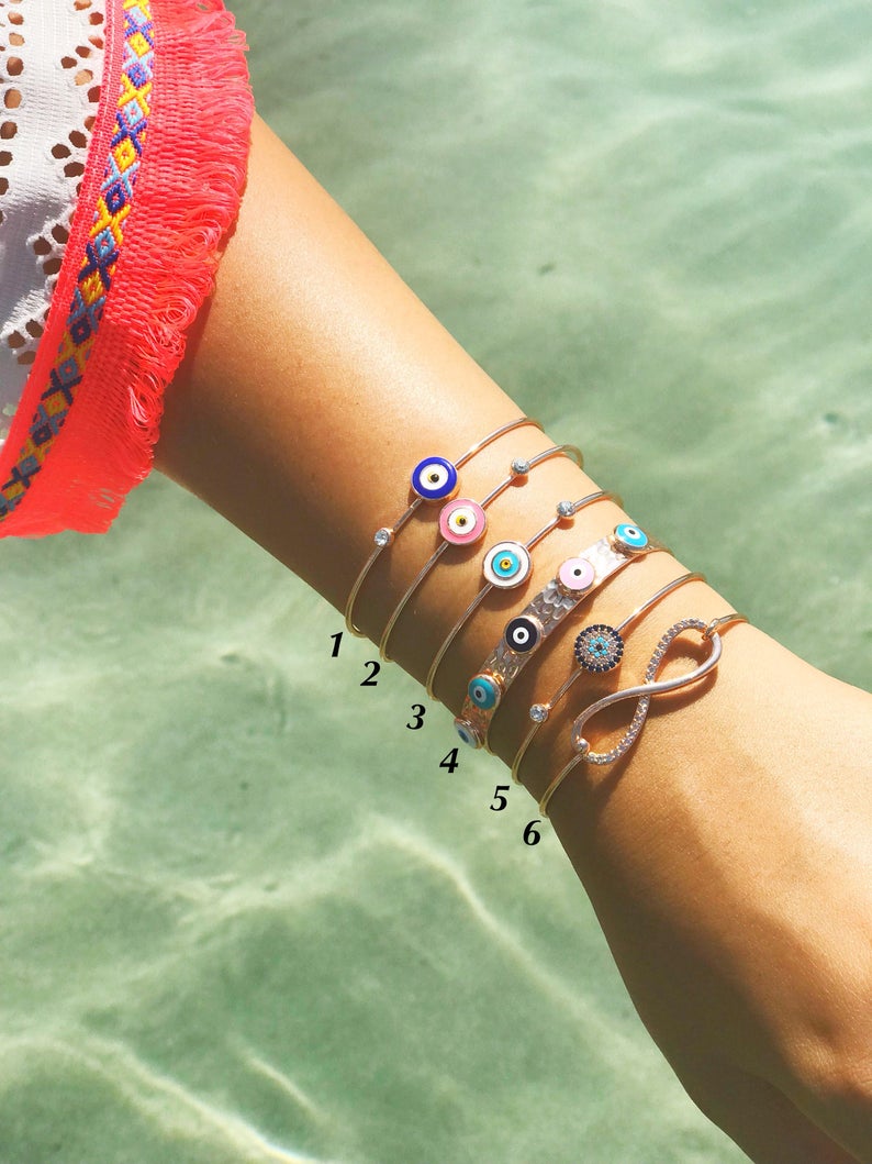 A beautiful rose gold bangle bracelet featuring a movable blue evil eye charm, showcasing its elegant design and adjustable fit.