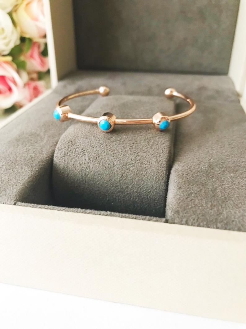 A beautiful rose gold bangle bracelet featuring turquoise beads and a movable oval evil eye charm, showcasing its elegant design.