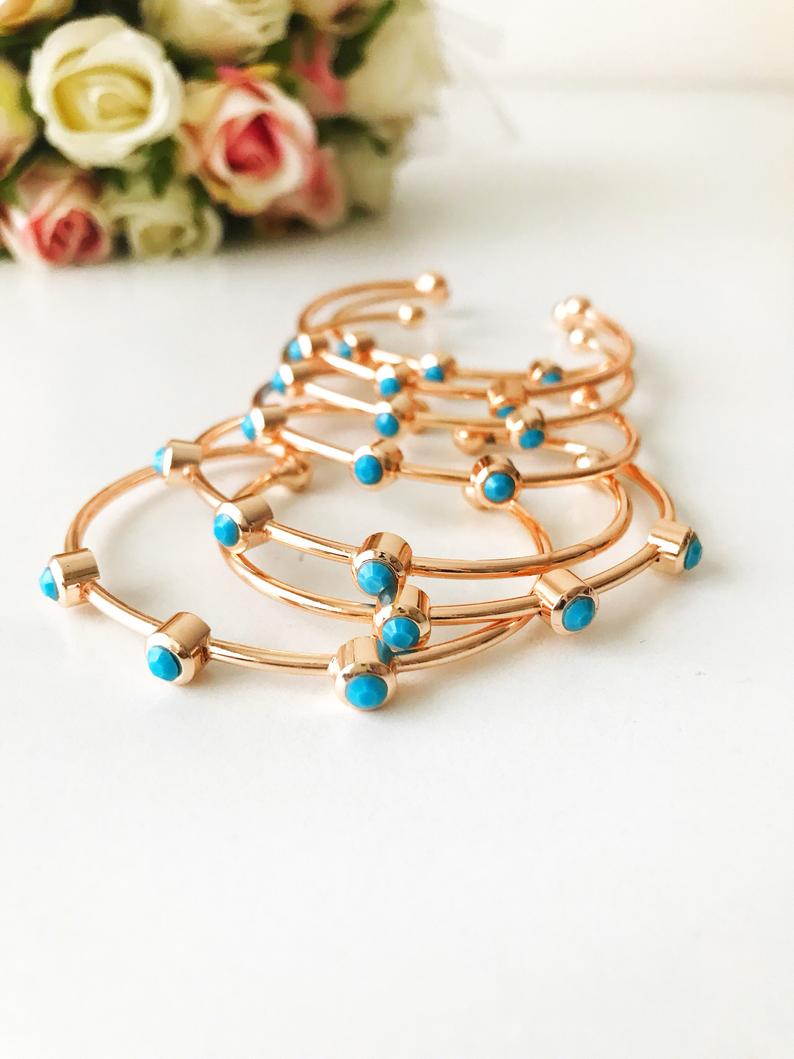 A beautiful rose gold bangle bracelet featuring turquoise beads and a movable oval evil eye charm, showcasing its elegant design.