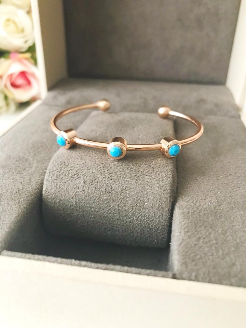 A beautiful rose gold bangle bracelet featuring turquoise beads and a movable oval evil eye charm, showcasing its elegant design.