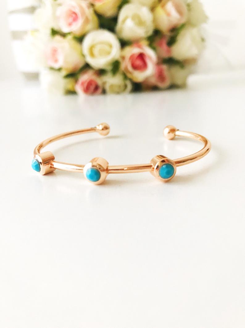 A beautiful rose gold bangle bracelet featuring turquoise beads and a movable oval evil eye charm, showcasing its elegant design.