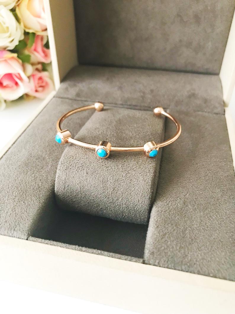 A beautiful rose gold bangle bracelet featuring turquoise beads and a movable oval evil eye charm, showcasing its elegant design.