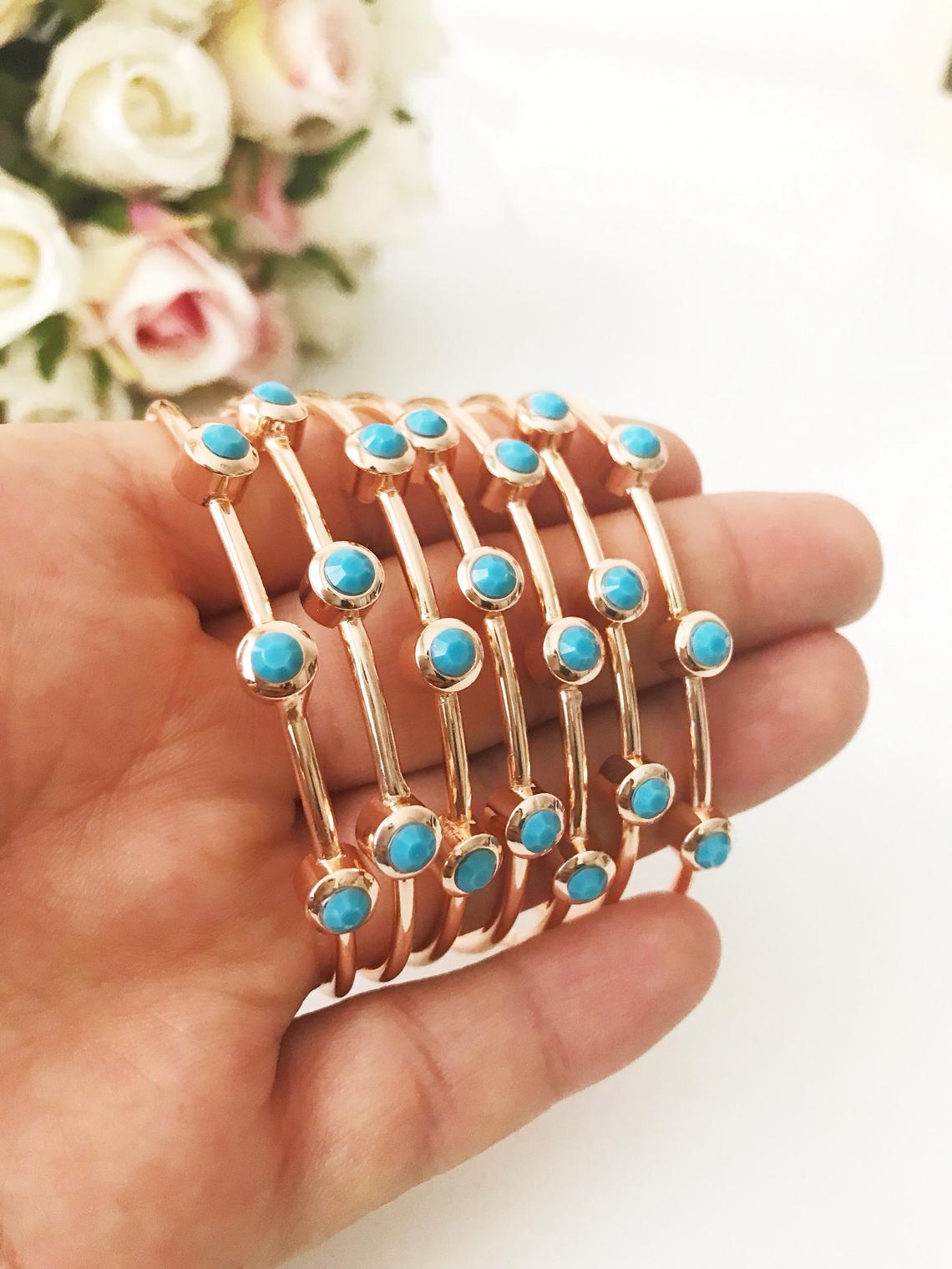 A beautiful rose gold bangle bracelet featuring turquoise beads and a movable oval evil eye charm, showcasing its elegant design.