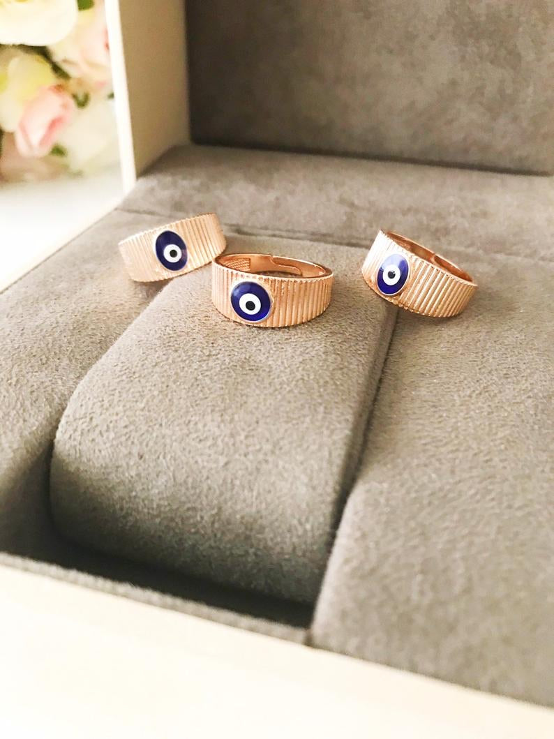 A dainty rose gold adjustable ring featuring an oval blue evil eye bead, symbolizing protection and style.