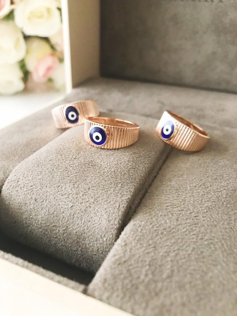 A dainty rose gold adjustable ring featuring an oval blue evil eye bead, symbolizing protection and style.