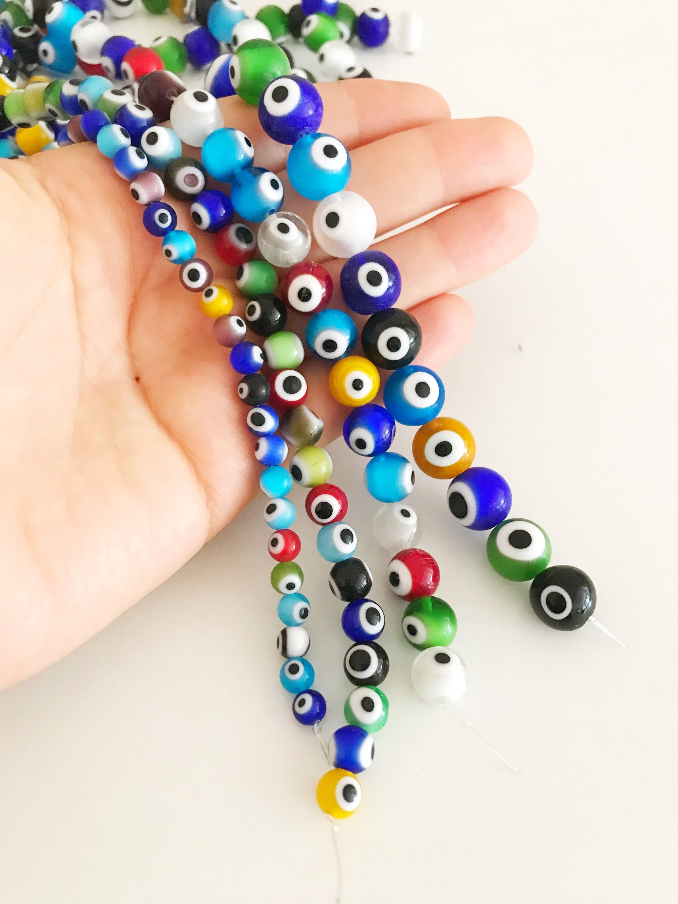 A collection of colorful round evil eye beads in various sizes, showcasing their vibrant colors and glass material, perfect for jewelry making.