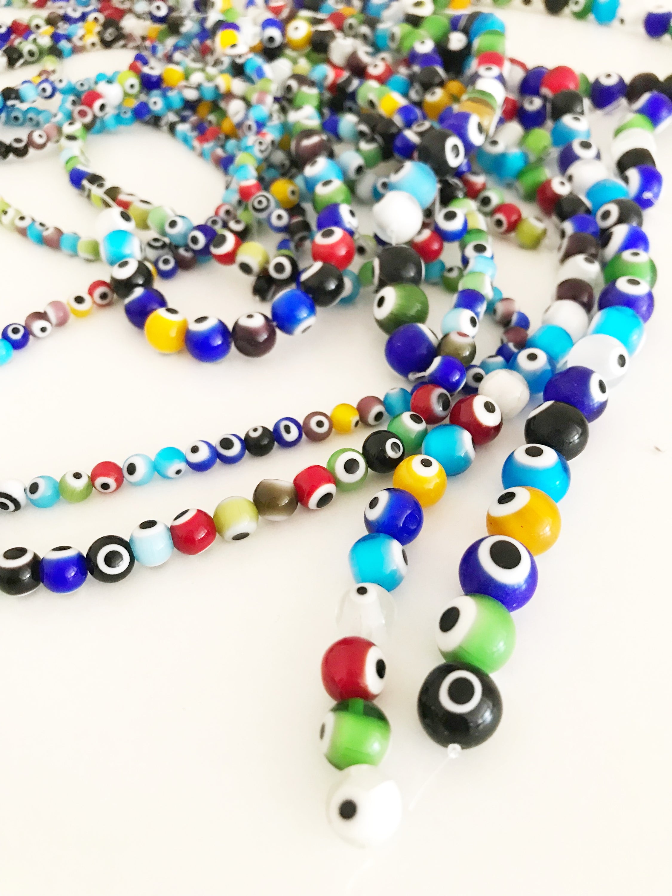 A collection of colorful round evil eye beads in various sizes, showcasing their vibrant colors and glass material, perfect for jewelry making.