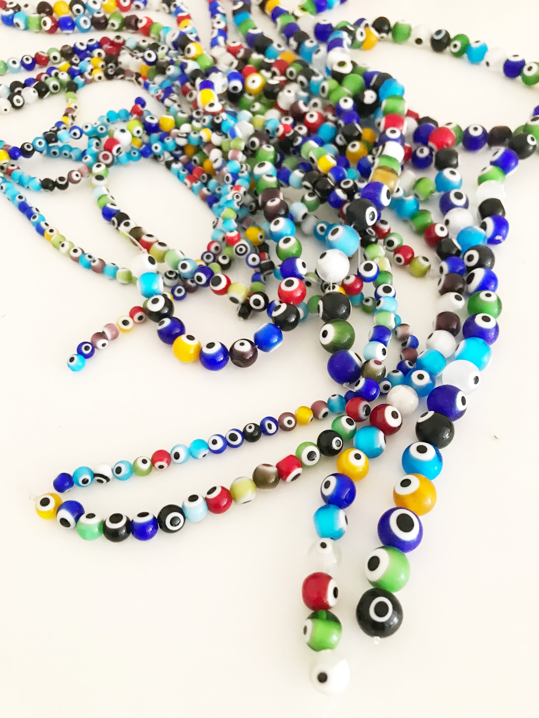 A collection of colorful round evil eye beads in various sizes, showcasing their vibrant colors and glass material, perfect for jewelry making.