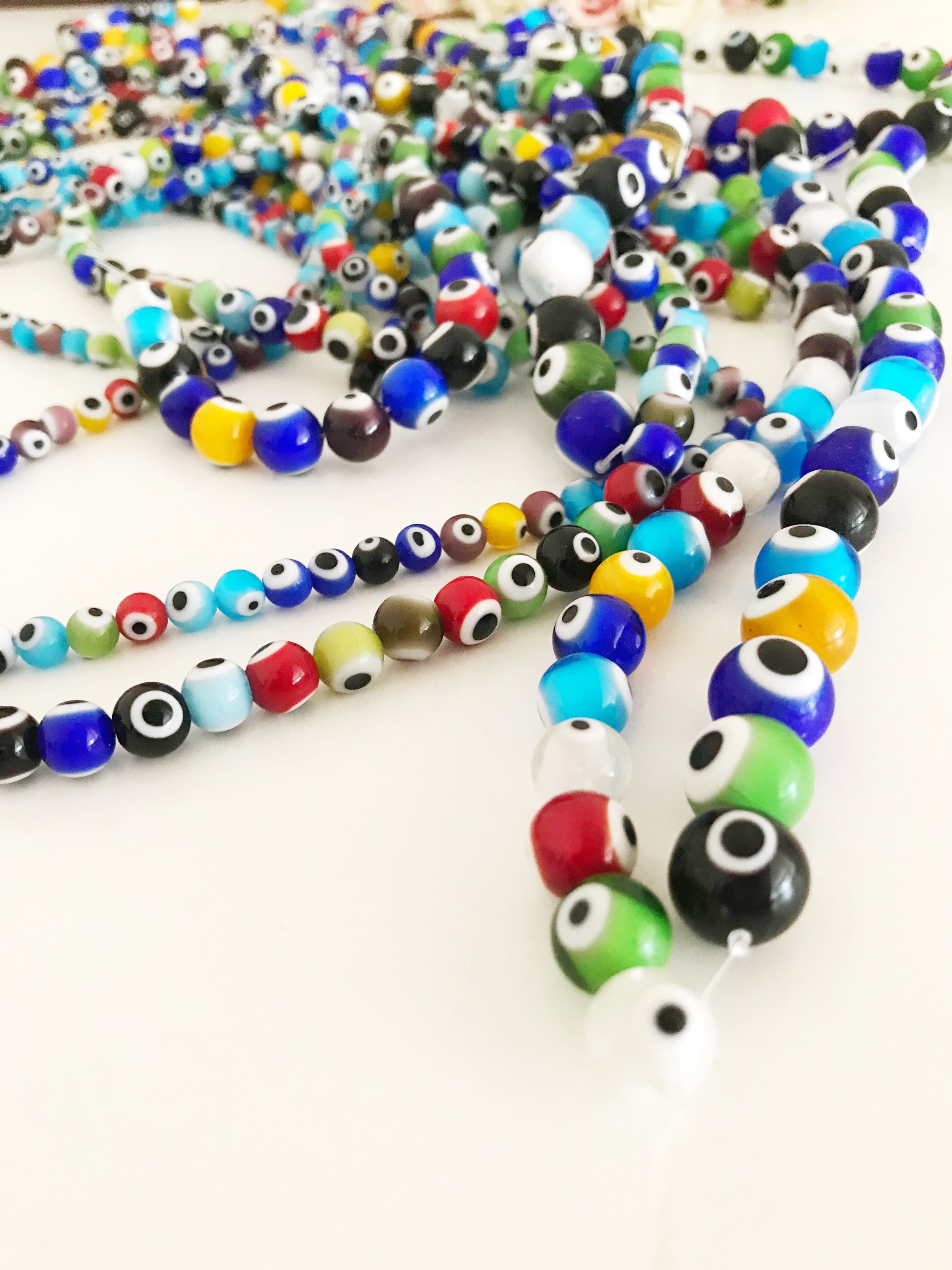 A collection of colorful round evil eye beads in various sizes, showcasing their vibrant colors and glass material, perfect for jewelry making.