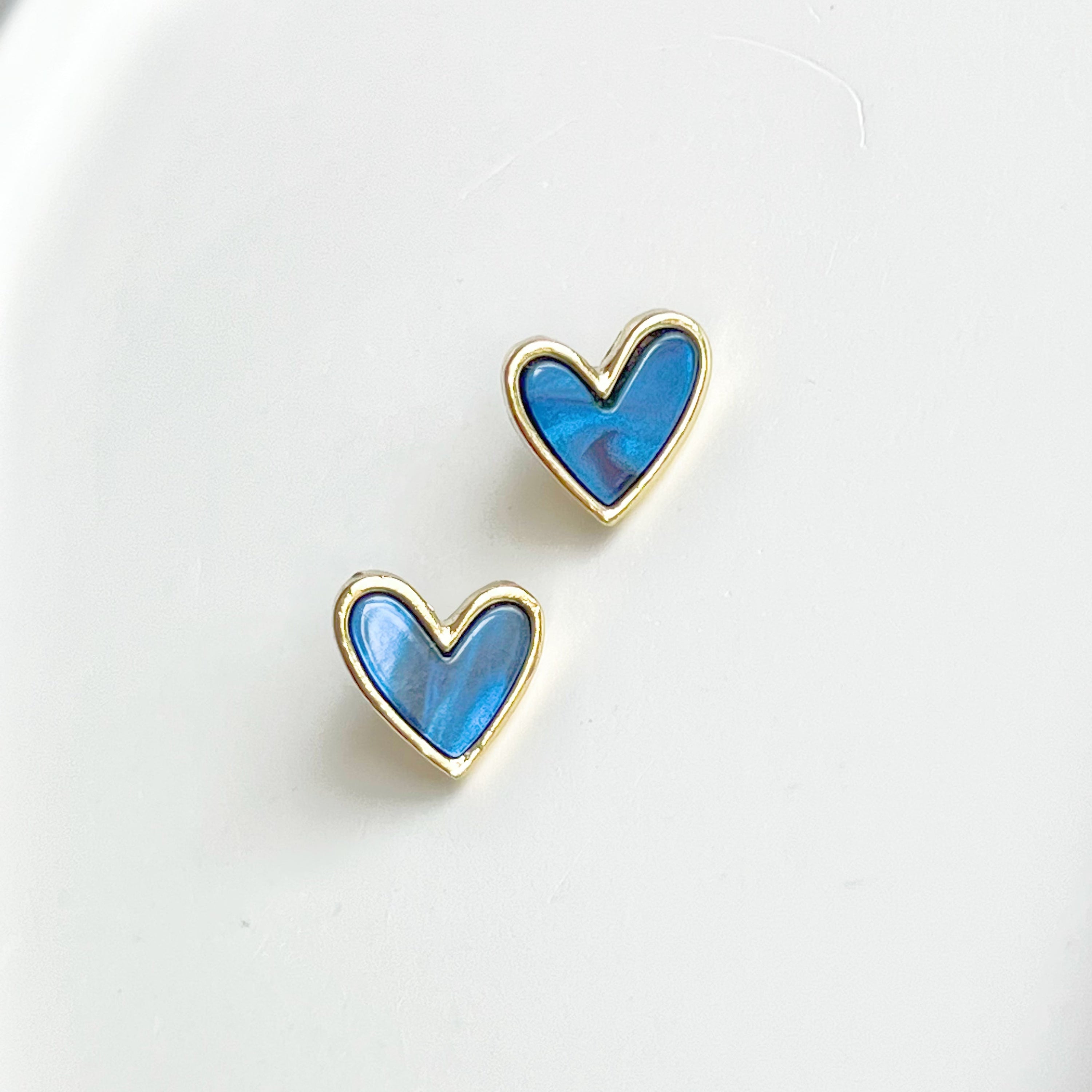 A pair of royal blue heart stud earrings with a gold color base, elegantly displayed in a gift box.