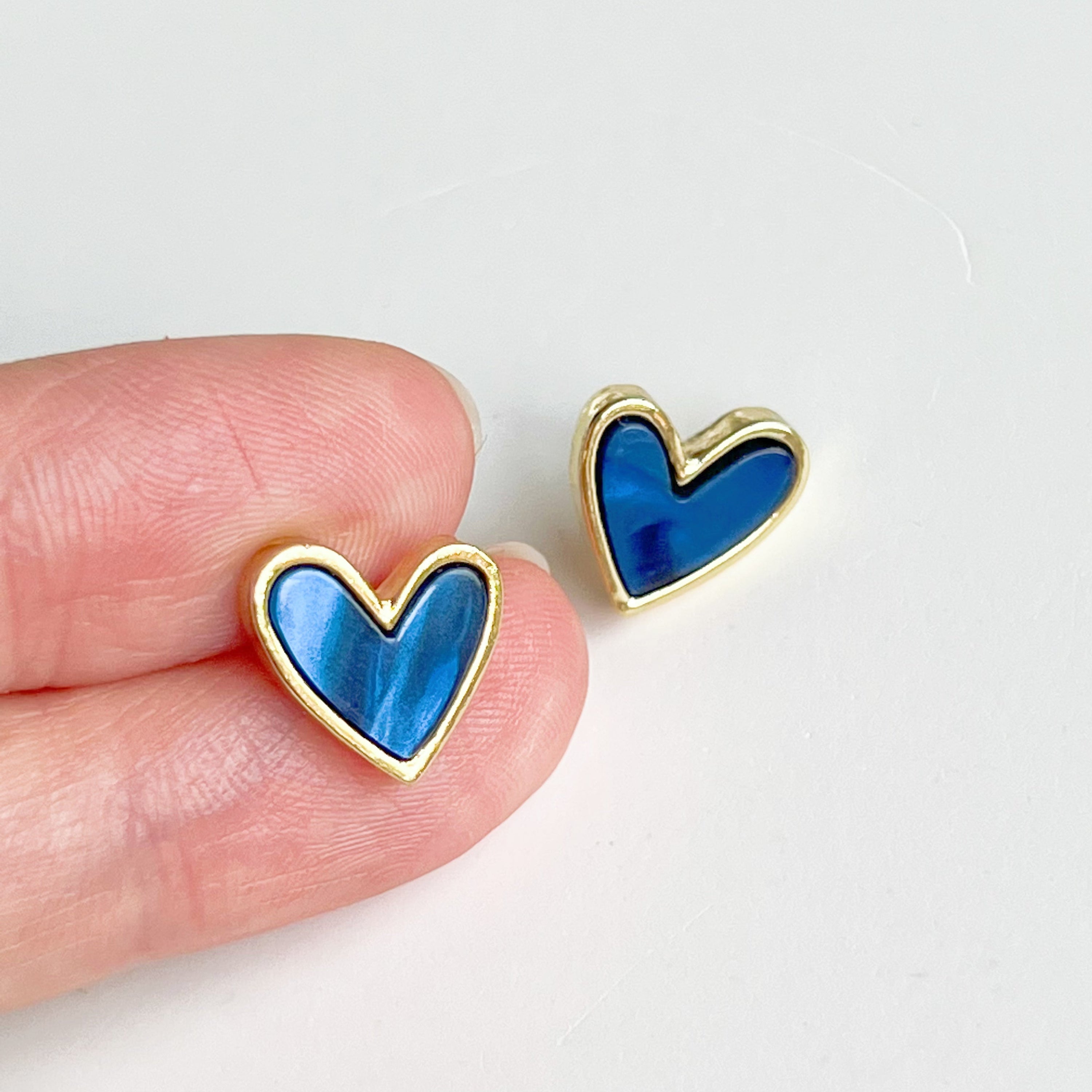 A pair of royal blue heart stud earrings with a gold color base, elegantly displayed in a gift box.