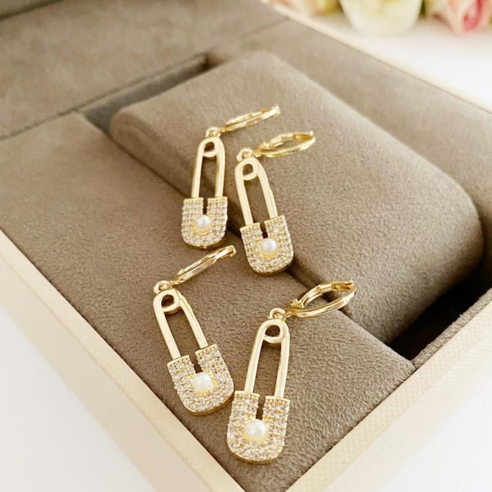 A pair of elegant gold safety pin hoop earrings, showcasing a unique design with a shiny finish, perfect for boho and modern styles.