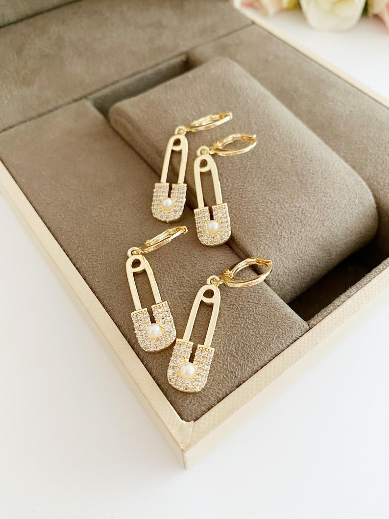 A pair of elegant gold safety pin hoop earrings, showcasing a unique design with a shiny finish, perfect for boho and modern styles.