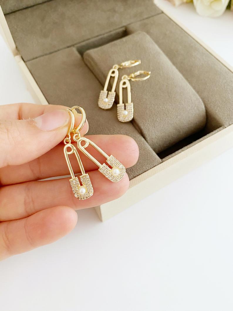 A pair of elegant gold safety pin hoop earrings, showcasing a unique design with a shiny finish, perfect for boho and modern styles.