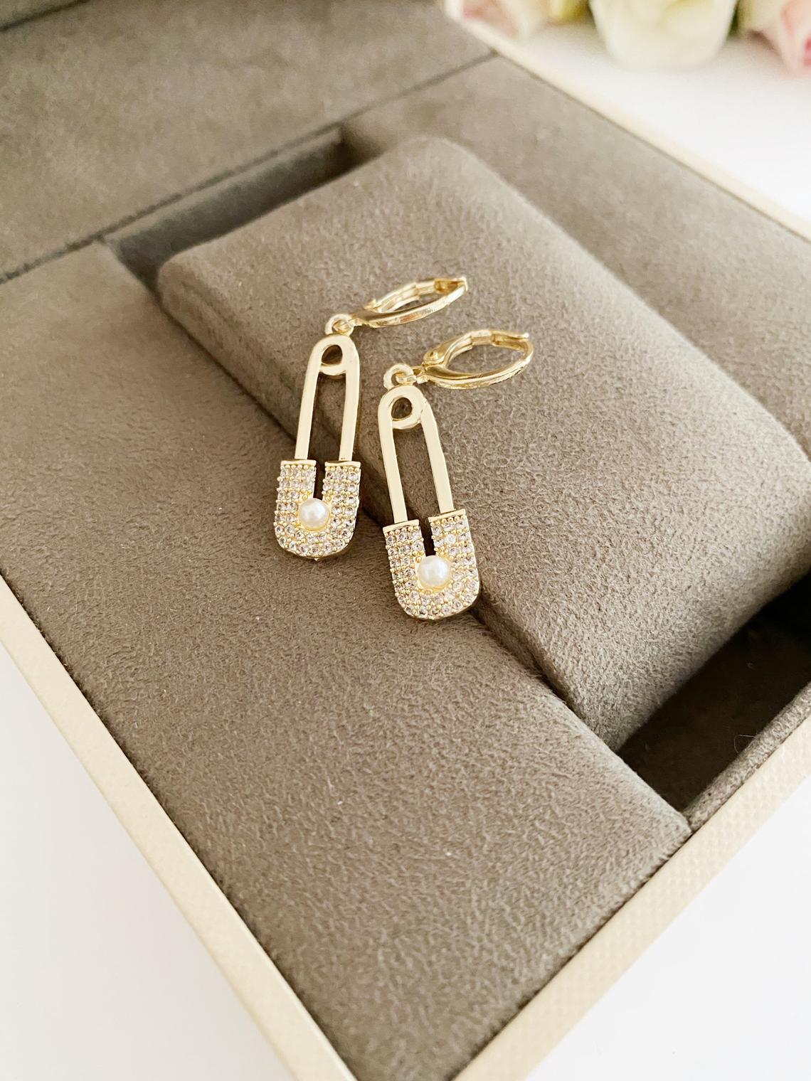 A pair of elegant gold safety pin hoop earrings, showcasing a unique design with a shiny finish, perfect for boho and modern styles.