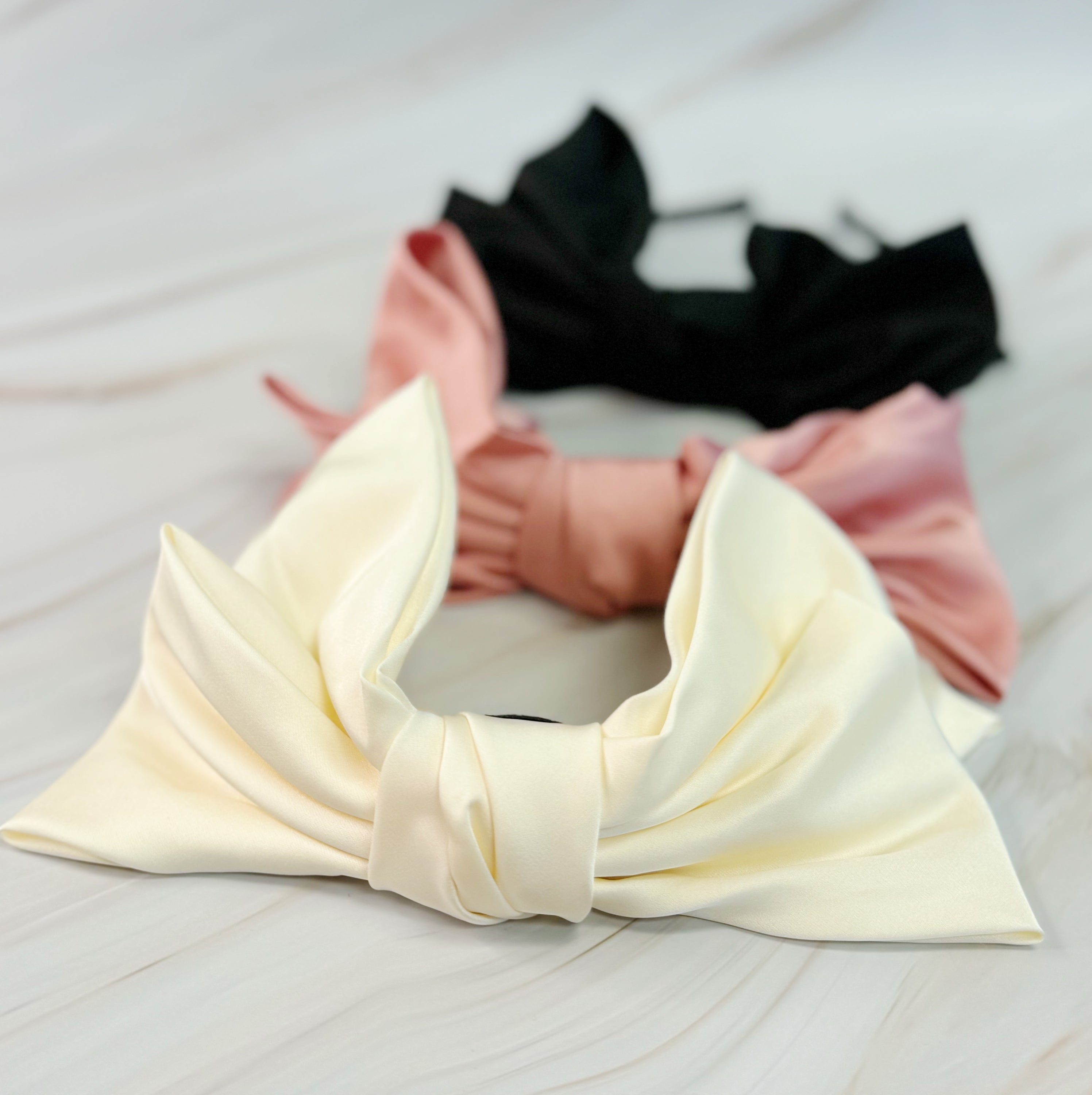 A stylish Satin Bow Crown Headband featuring a large doubled satin bow on a slim body, perfect for enhancing any outfit.