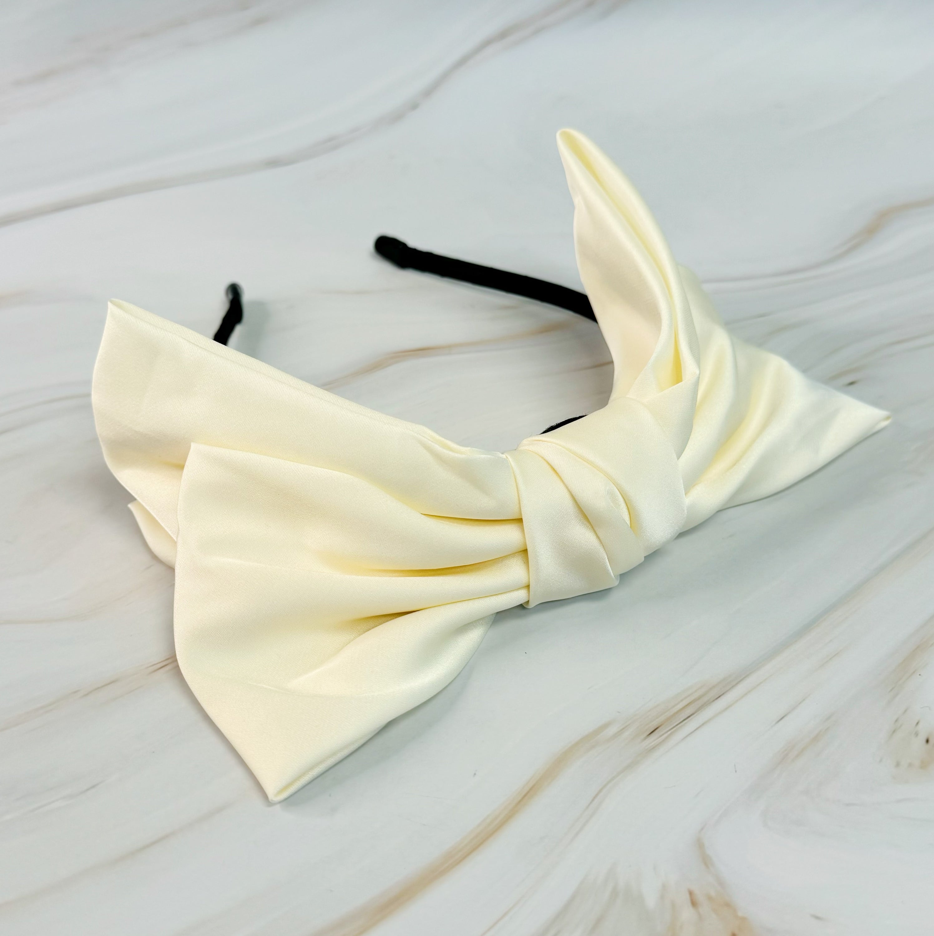 A stylish Satin Bow Crown Headband featuring a large doubled satin bow on a slim body, perfect for enhancing any outfit.