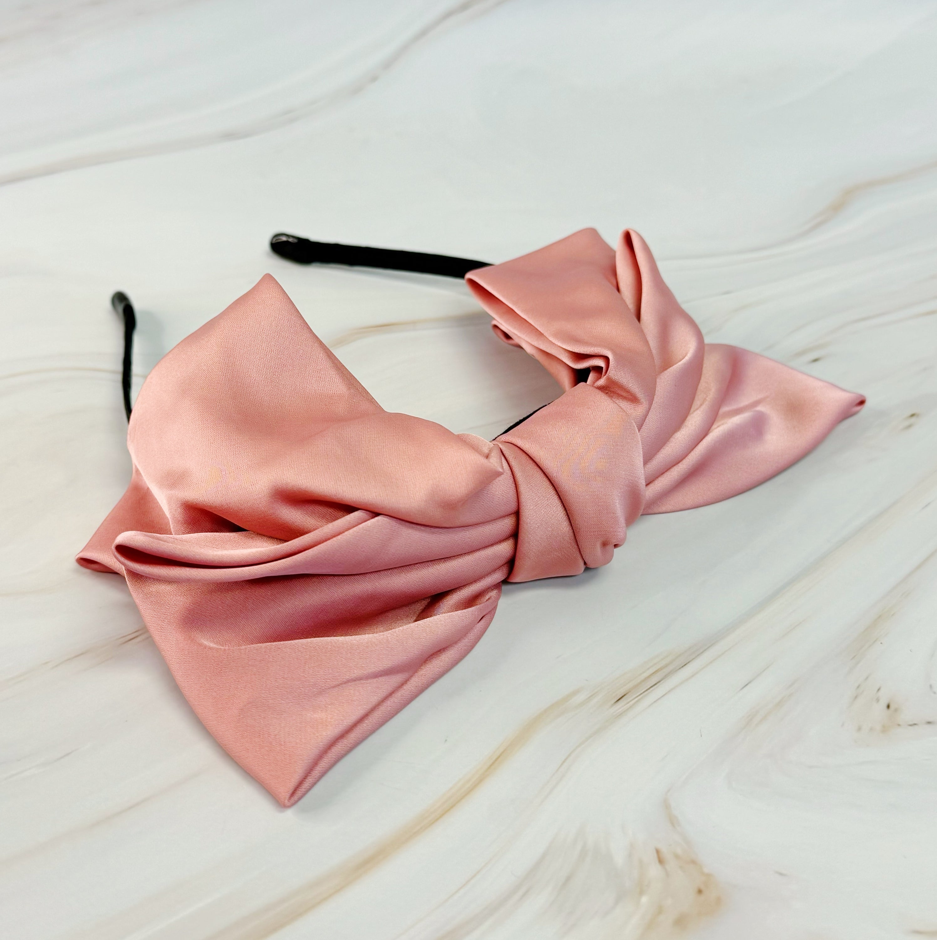 A stylish Satin Bow Crown Headband featuring a large doubled satin bow on a slim body, perfect for enhancing any outfit.