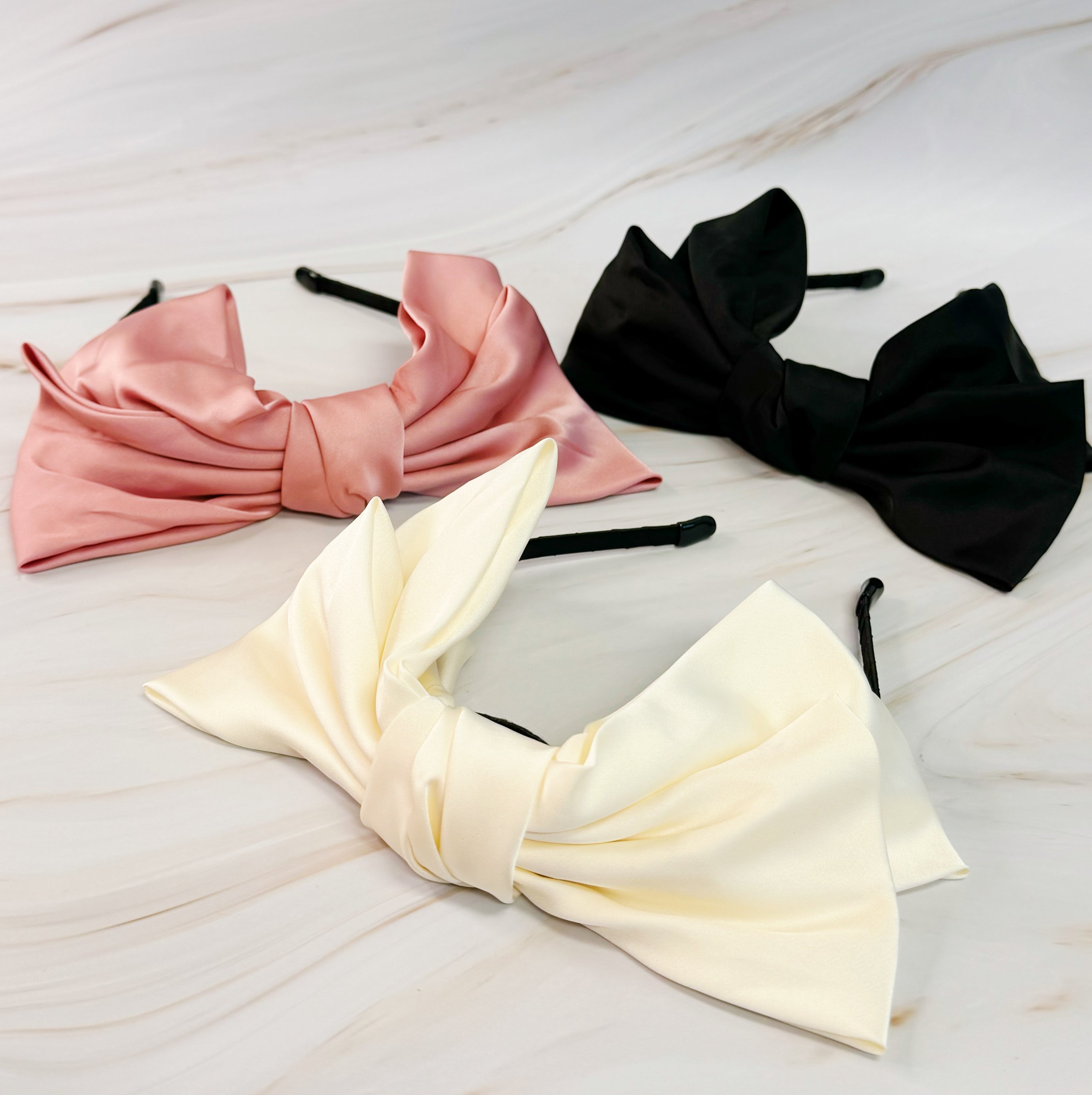 A stylish Satin Bow Crown Headband featuring a large doubled satin bow on a slim body, perfect for enhancing any outfit.