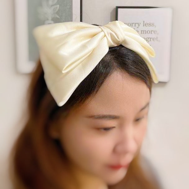 A stylish Satin Bow Crown Headband featuring a large doubled satin bow on a slim body, perfect for enhancing any outfit.