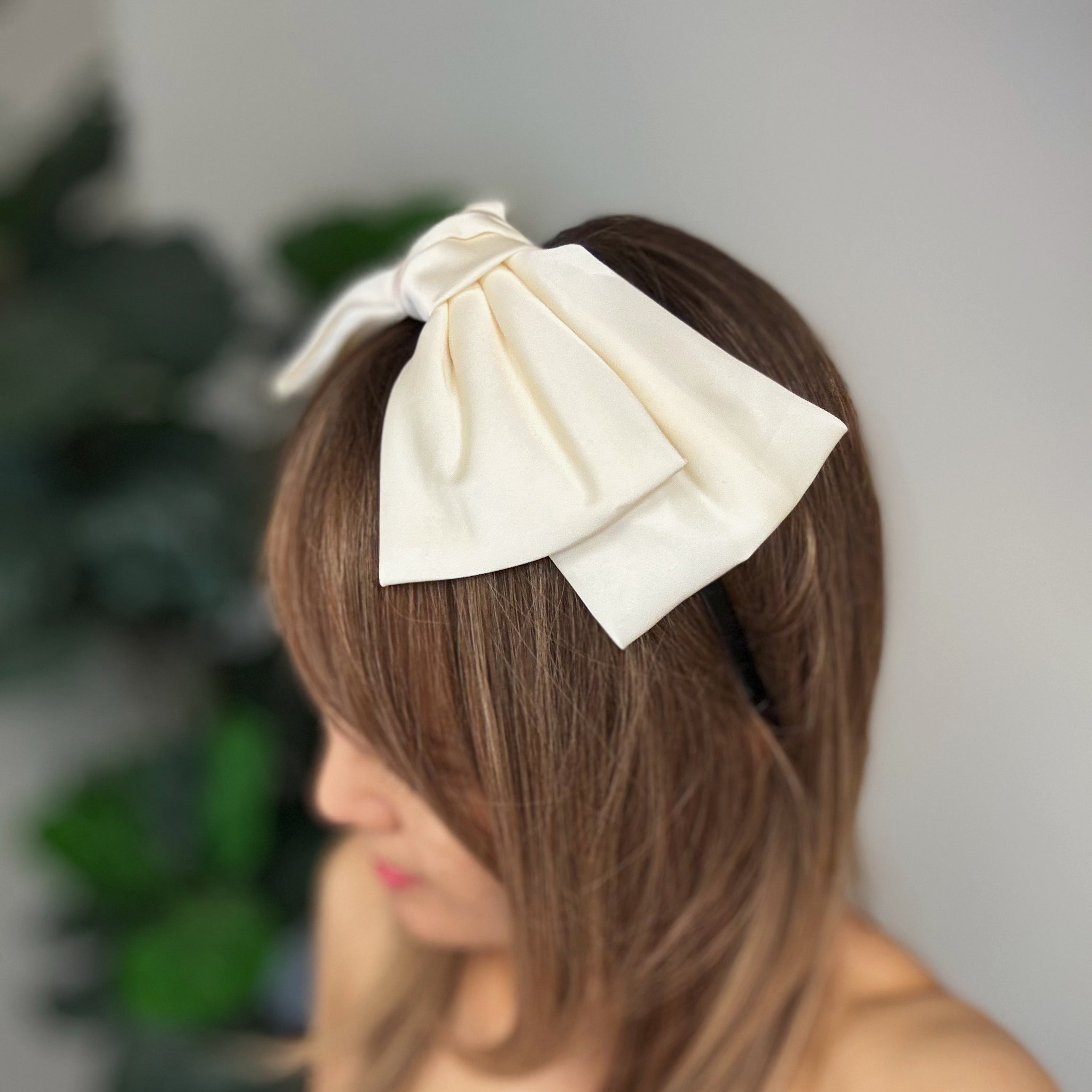 A stylish Satin Bow Crown Headband featuring a large doubled satin bow on a slim body, perfect for enhancing any outfit.