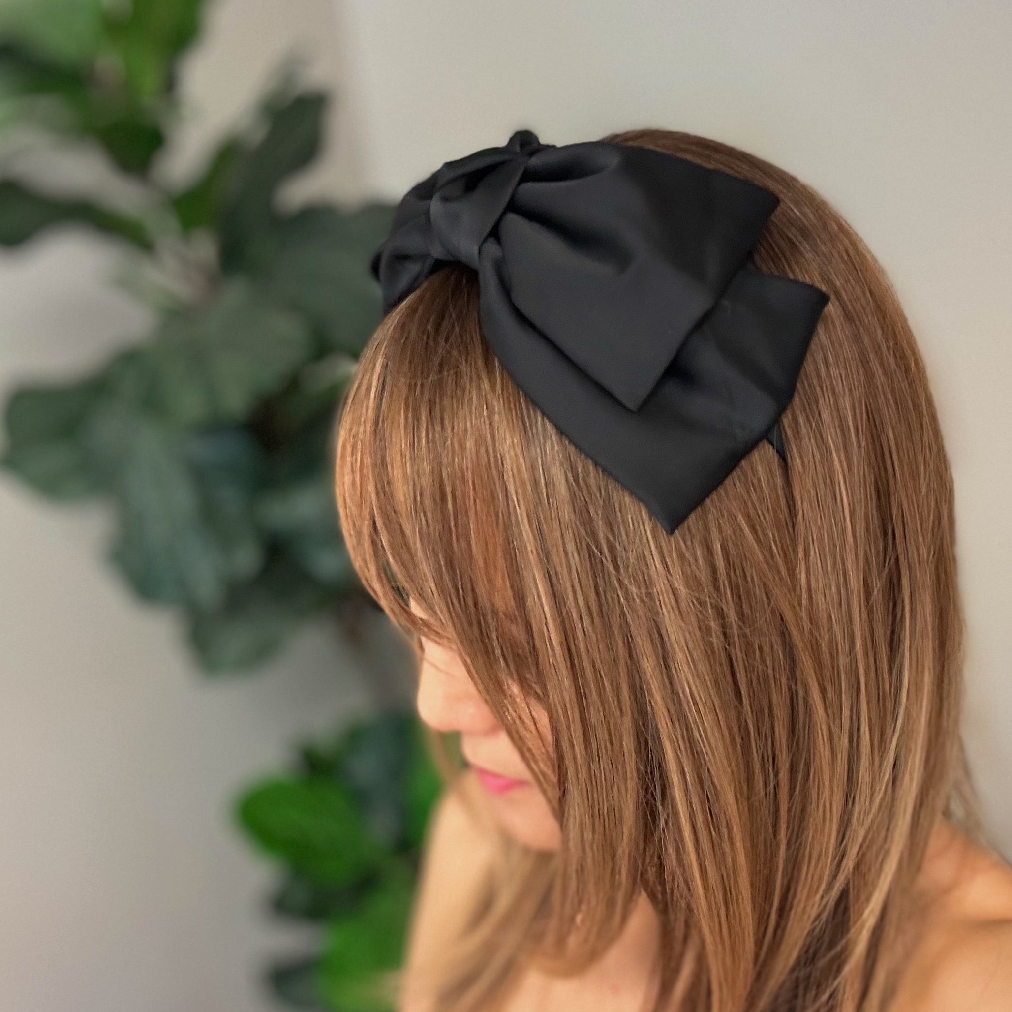 A stylish Satin Bow Crown Headband featuring a large doubled satin bow on a slim body, perfect for enhancing any outfit.