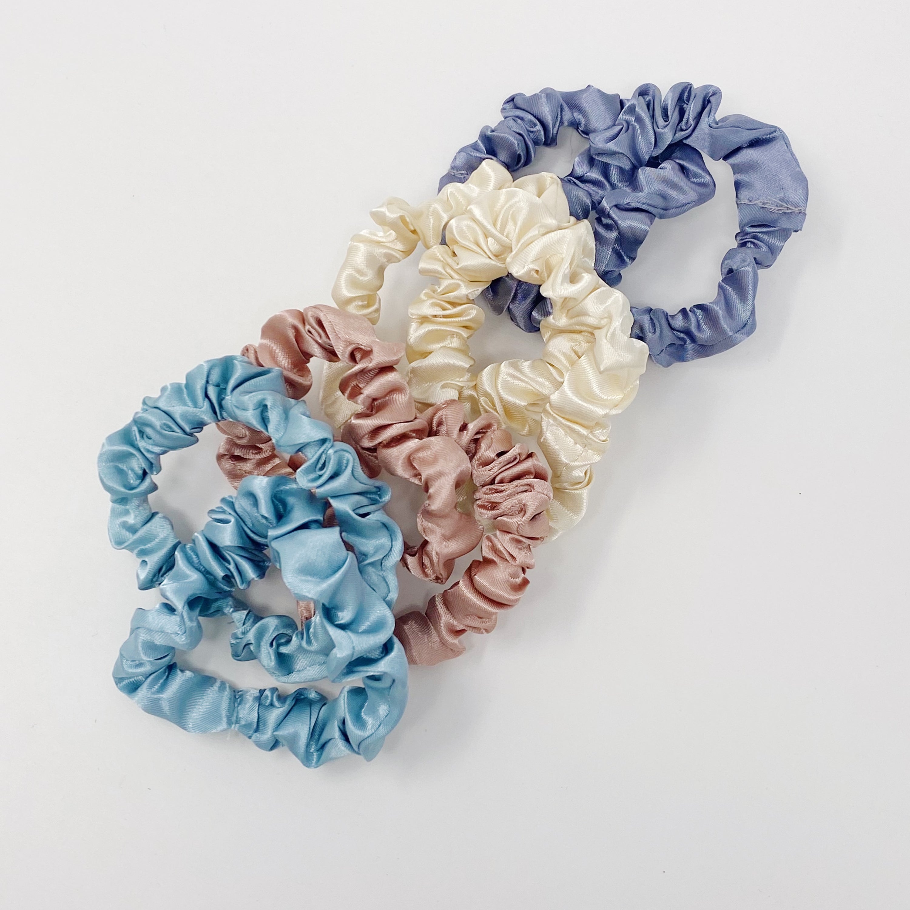 A set of 8 satin scrunchies in soft colors, elegantly displayed in transparent packaging with an Ellison + Young sticker.