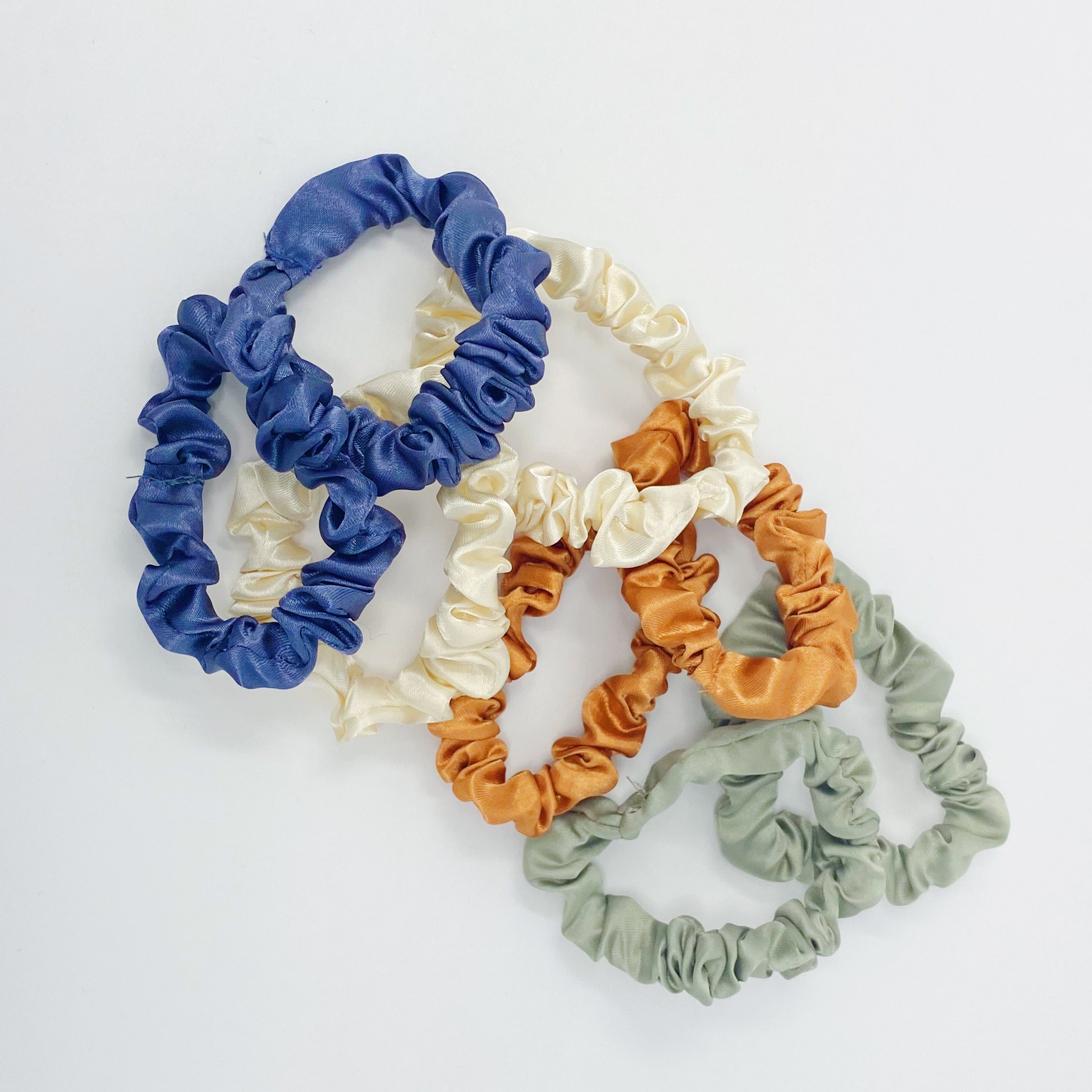 A set of 8 satin scrunchies in soft colors, elegantly displayed in transparent packaging with an Ellison + Young sticker.