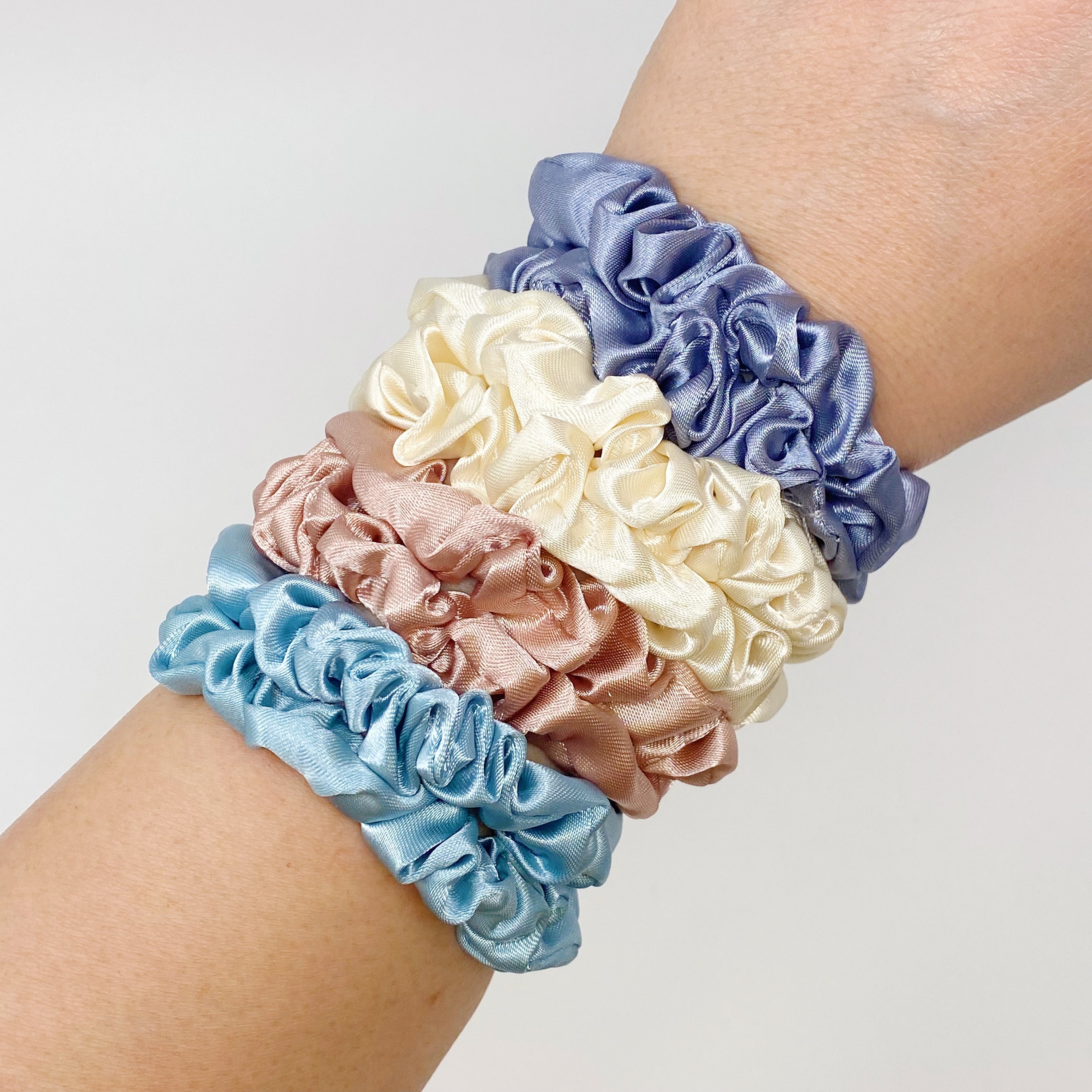 A set of 8 satin scrunchies in soft colors, elegantly displayed in transparent packaging with an Ellison + Young sticker.