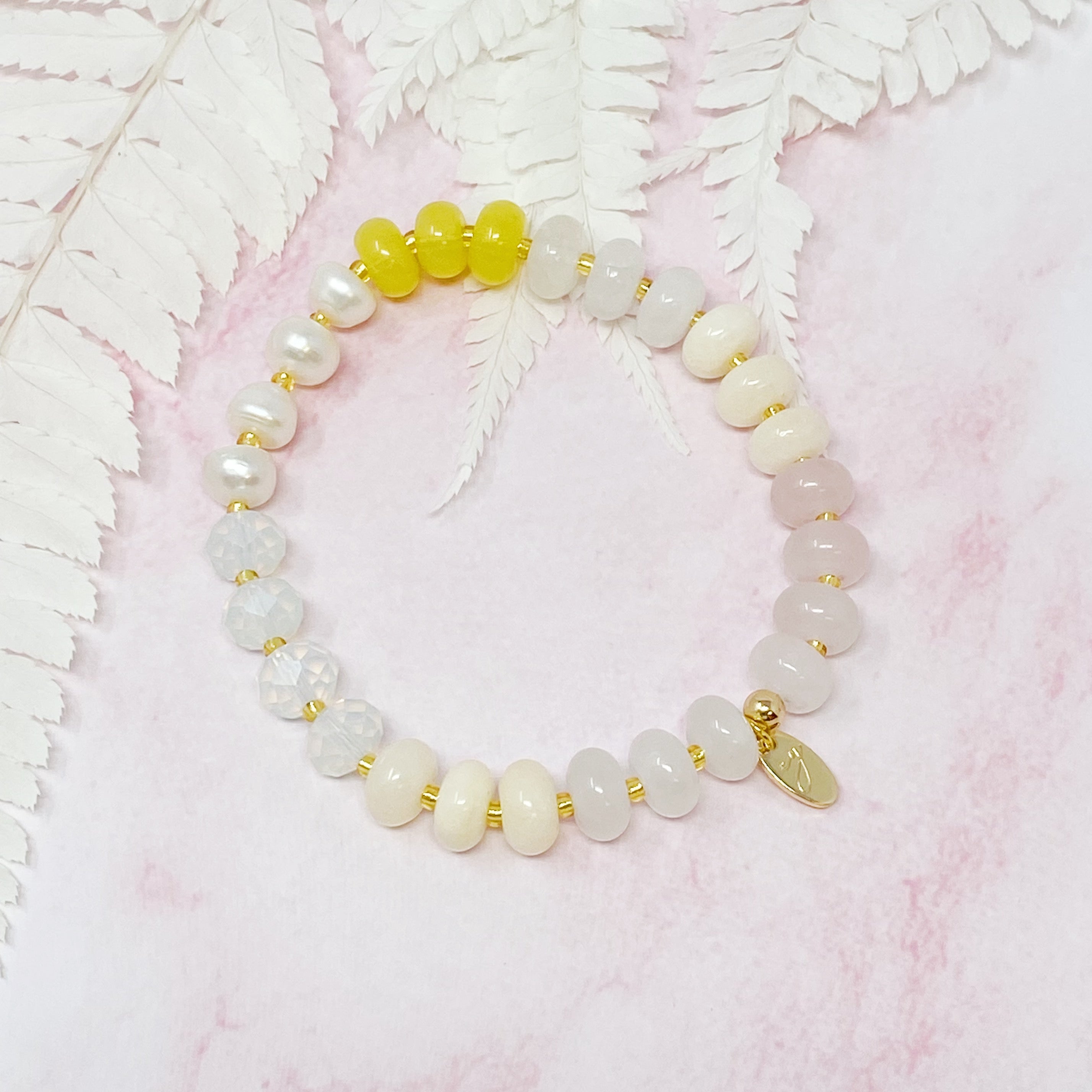 A stylish Semi-Precious Bauble Stretch Bracelet featuring natural stones, beads, and freshwater pearls with a golden logo tag.