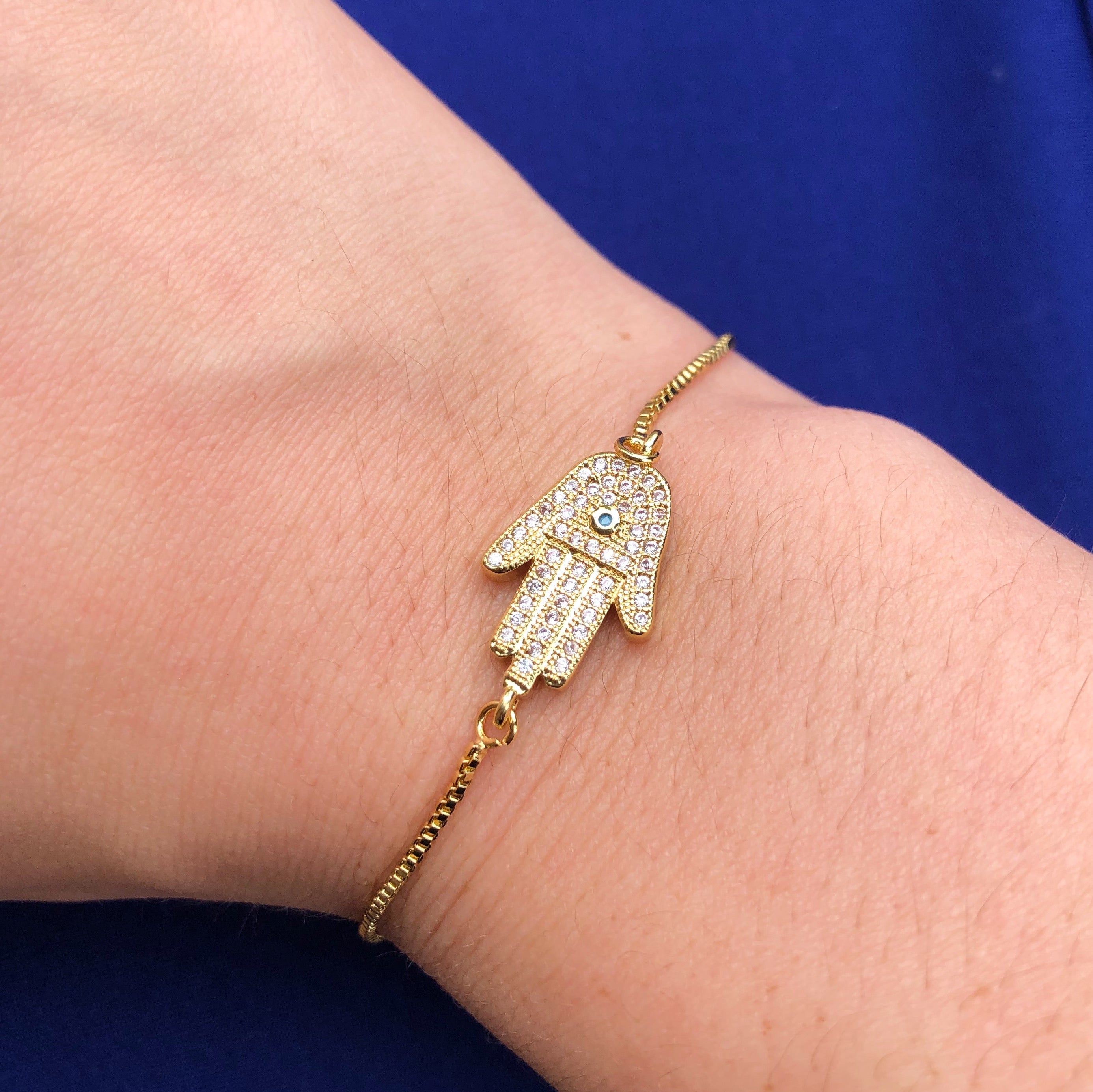 Serenity Hamsa Hand Slide Bracelet with jeweled evil eye charm, adjustable drawstring, and plated brass material.