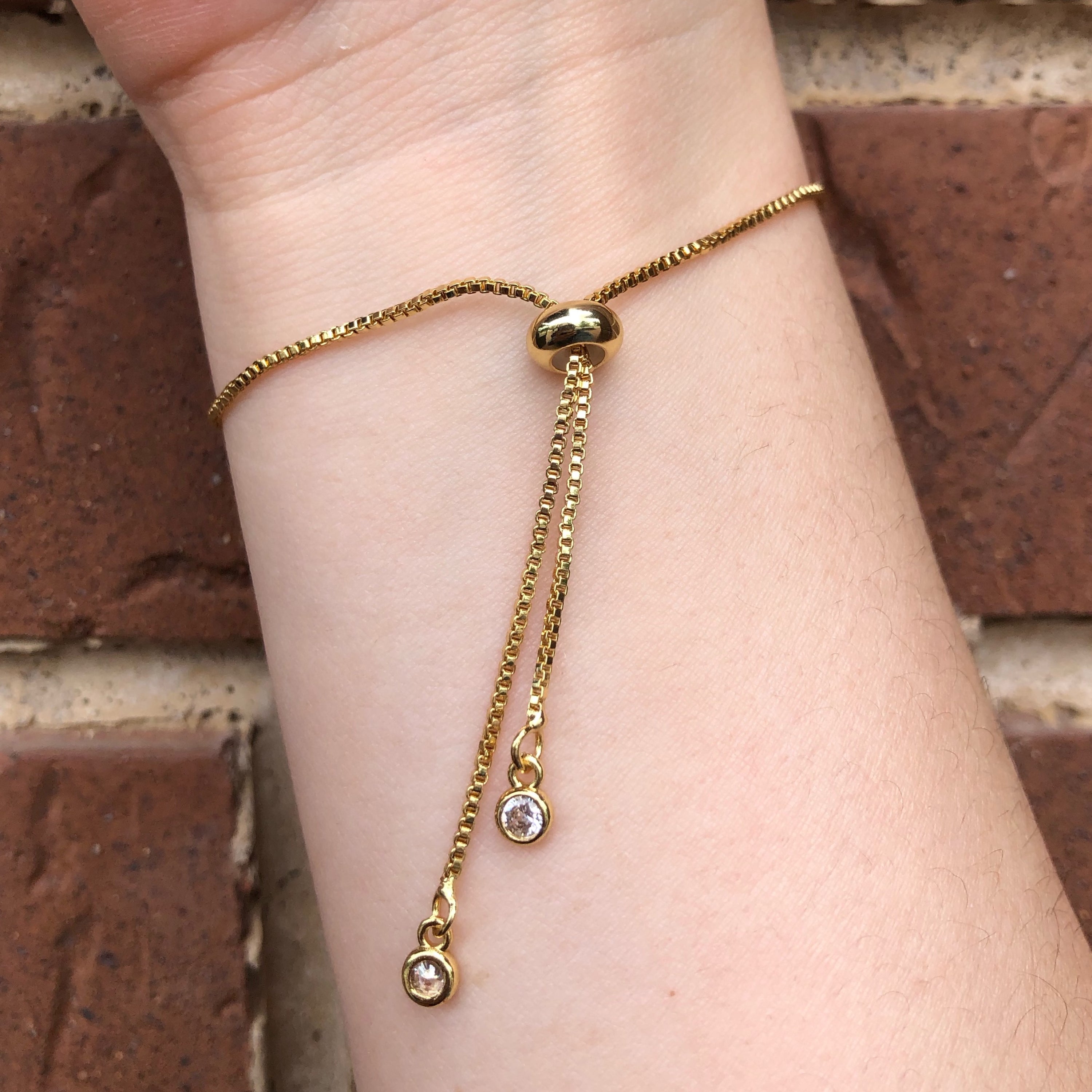 Serenity Hamsa Hand Slide Bracelet with jeweled evil eye charm, adjustable drawstring, and plated brass material.