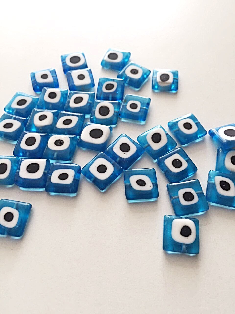 Set of 30 flat square glass evil eye beads in turquoise and dark blue, perfect for jewelry making.