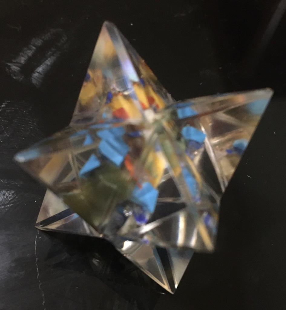 A Seven Chakra Orgone Merkaba made of translucent resin with seven colorful chakra gemstone chips, shaped like an eight-pointed star.