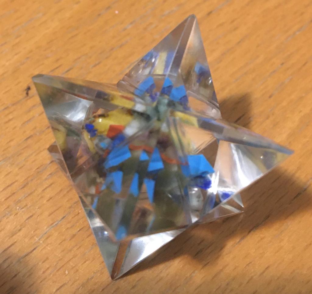 A Seven Chakra Orgone Merkaba made of translucent resin with seven colorful chakra gemstone chips, shaped like an eight-pointed star.