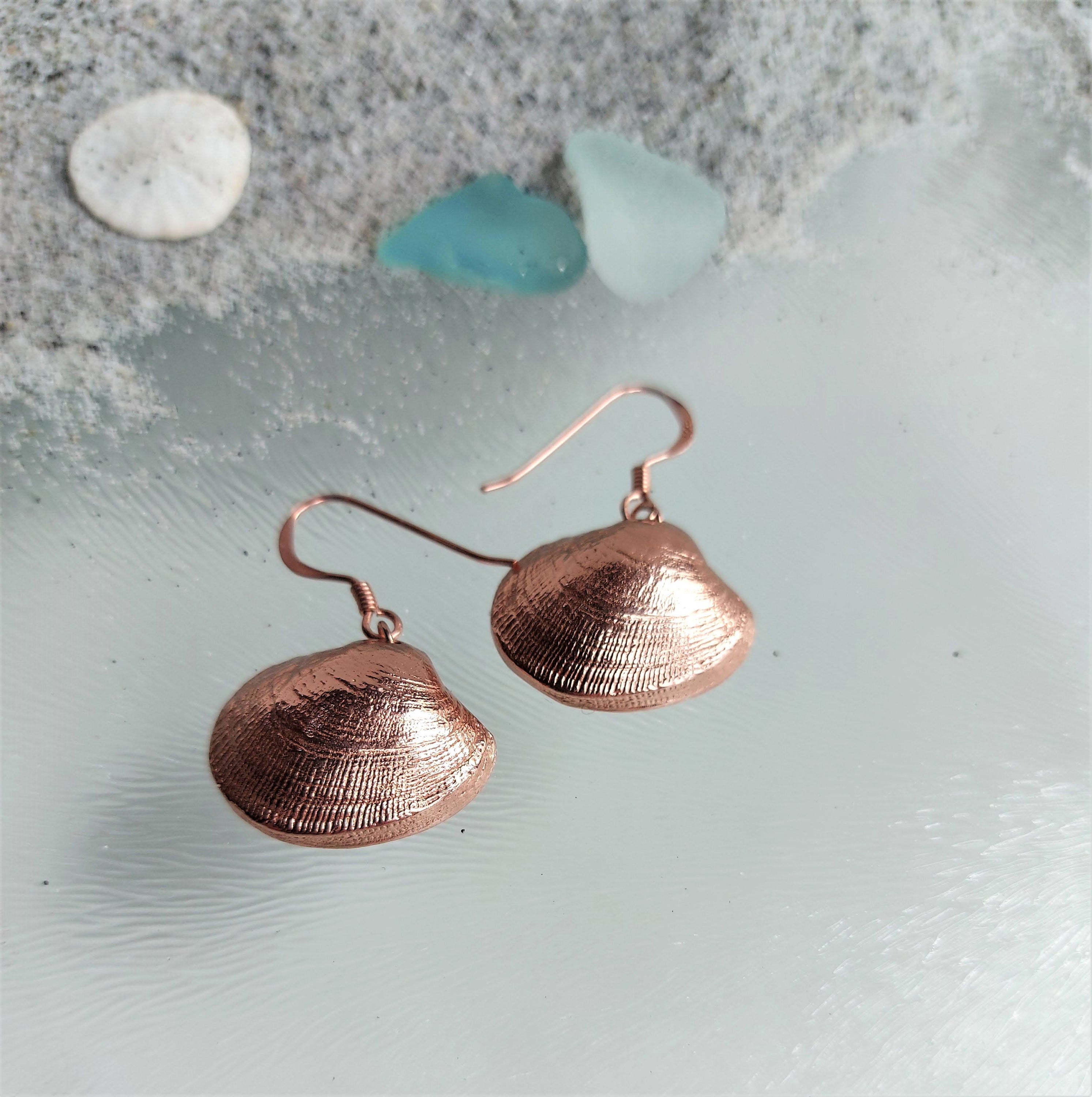 A pair of elegant silver seashell dangle earrings, showcasing intricate detailing and a shiny finish, perfect for ocean lovers.