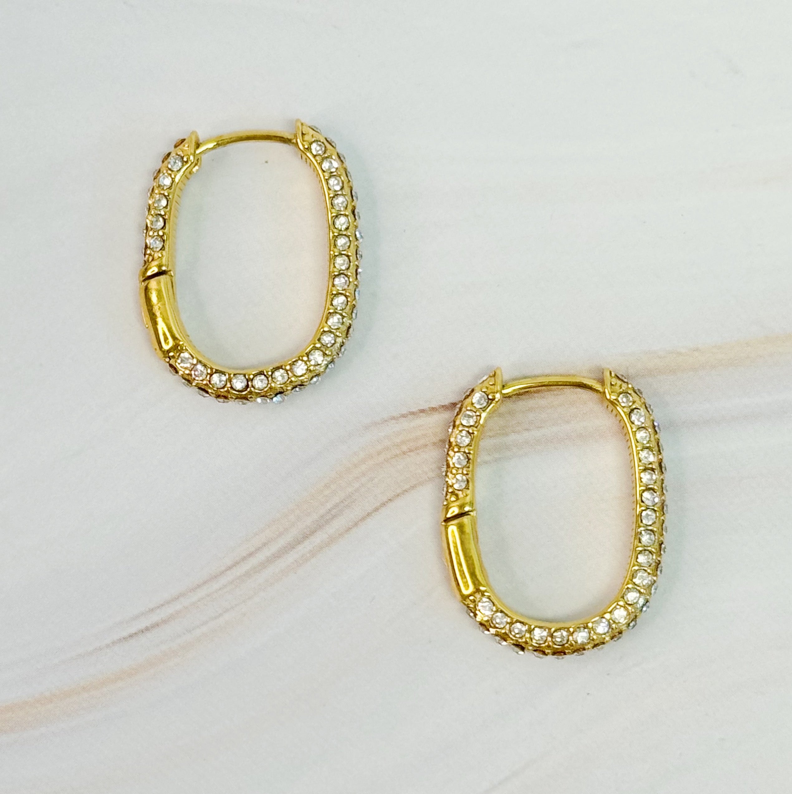 Sophisticated Shine Covered Oval Hoop Earrings in 18k gold plated stainless steel, showcasing their elegant oval shape and shiny finish.