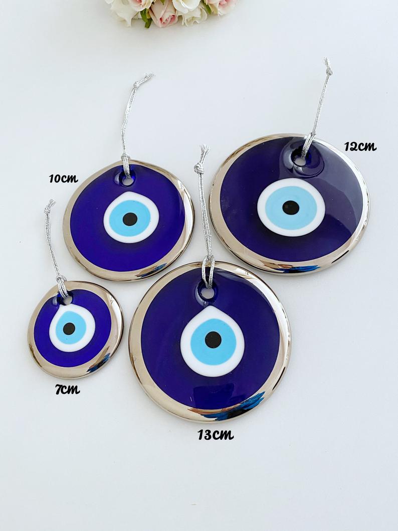 A collection of handmade silver evil eye beads ranging from 7cm to 13cm, showcasing intricate designs and a shiny finish, ready for wall hanging.